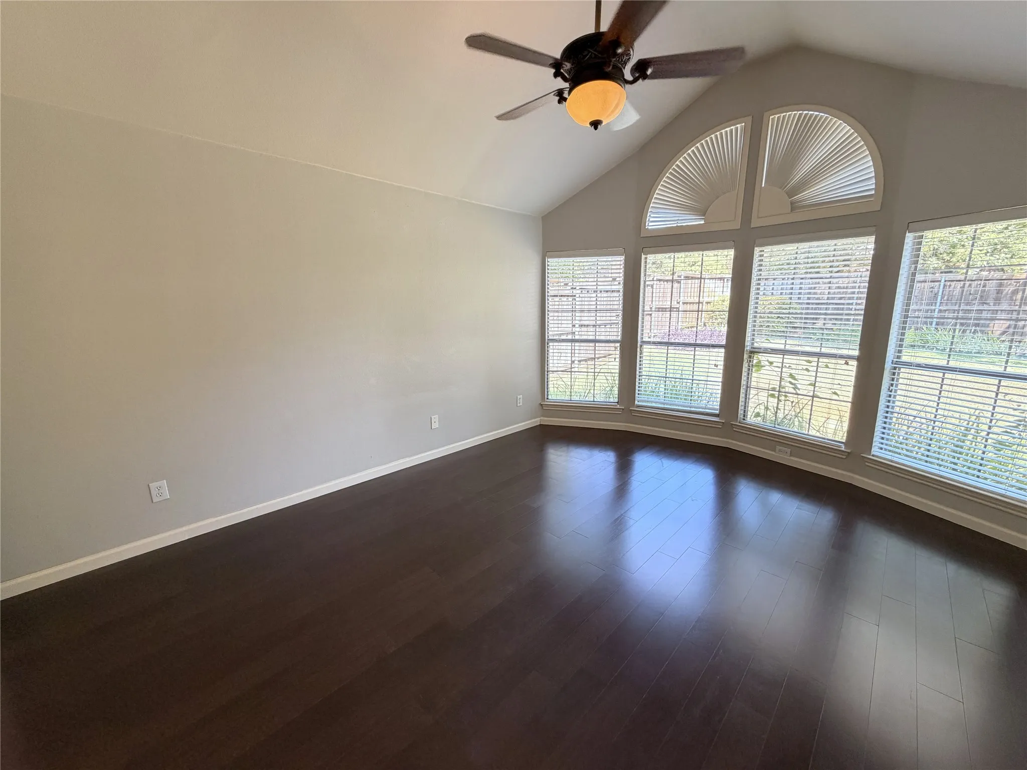 Vaulted ceiling featuring a ceiling fan, dark wood-finish flooring, and a bay window with arched transom windows