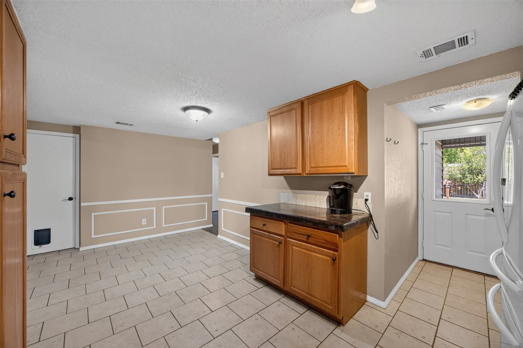 Light wood-finish cabinetry with dark countertops, tiled flooring, and a paneled accent wall