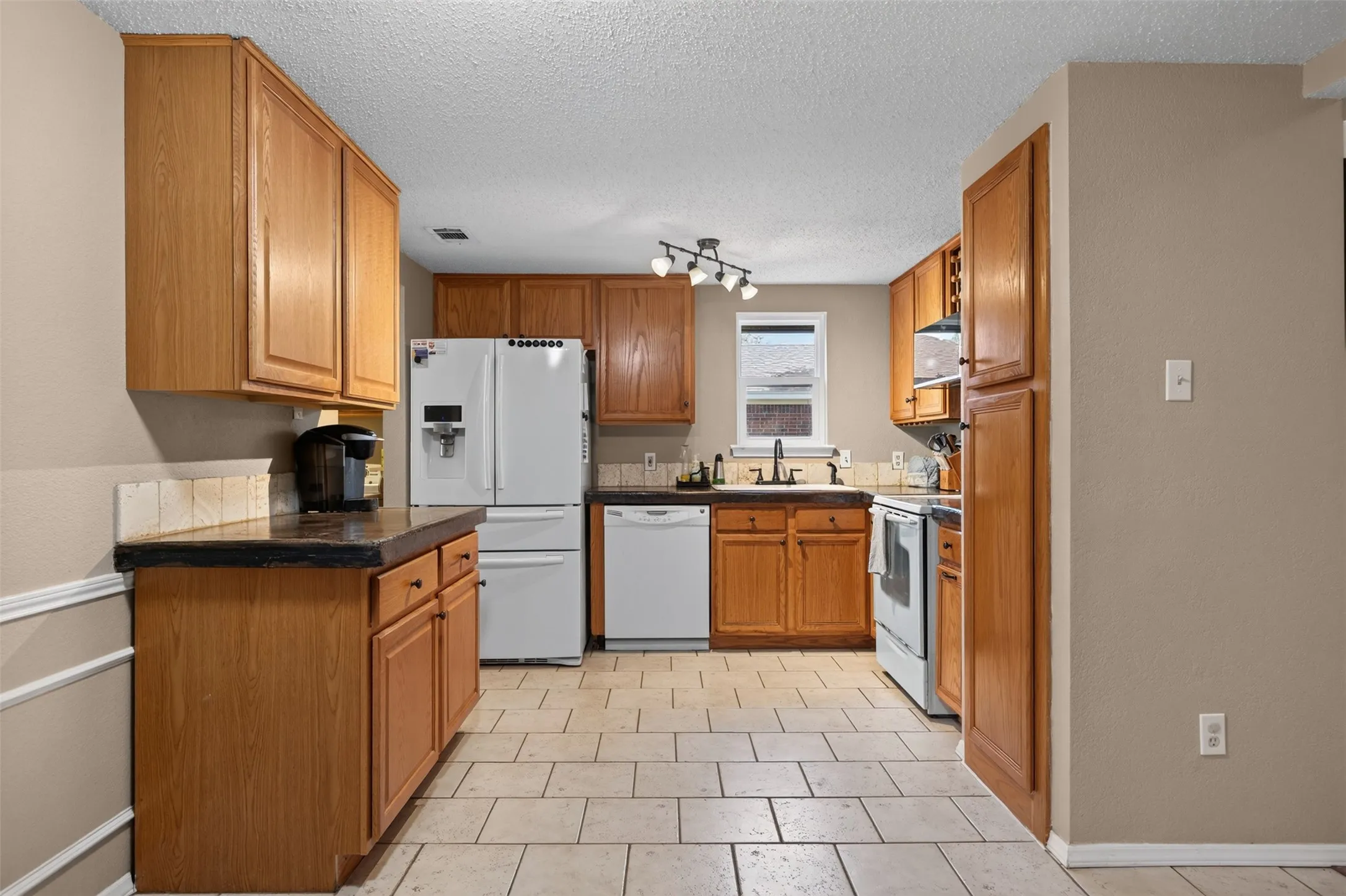 Kitchen featuring wood cabinetry, white appliances, tile flooring, and dark countertops