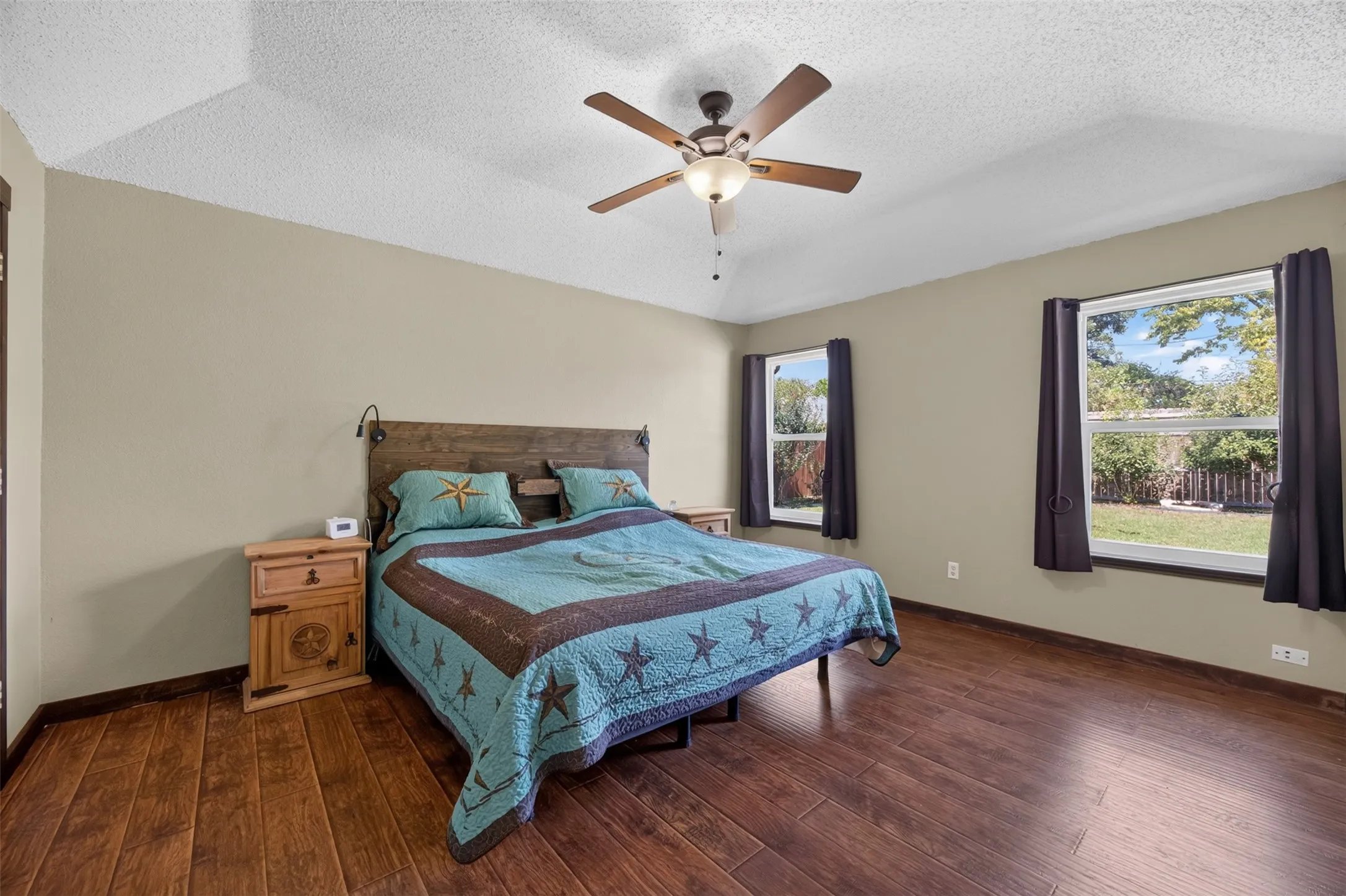 Vaulted ceiling with a ceiling fan, two windows, and wood-finish flooring