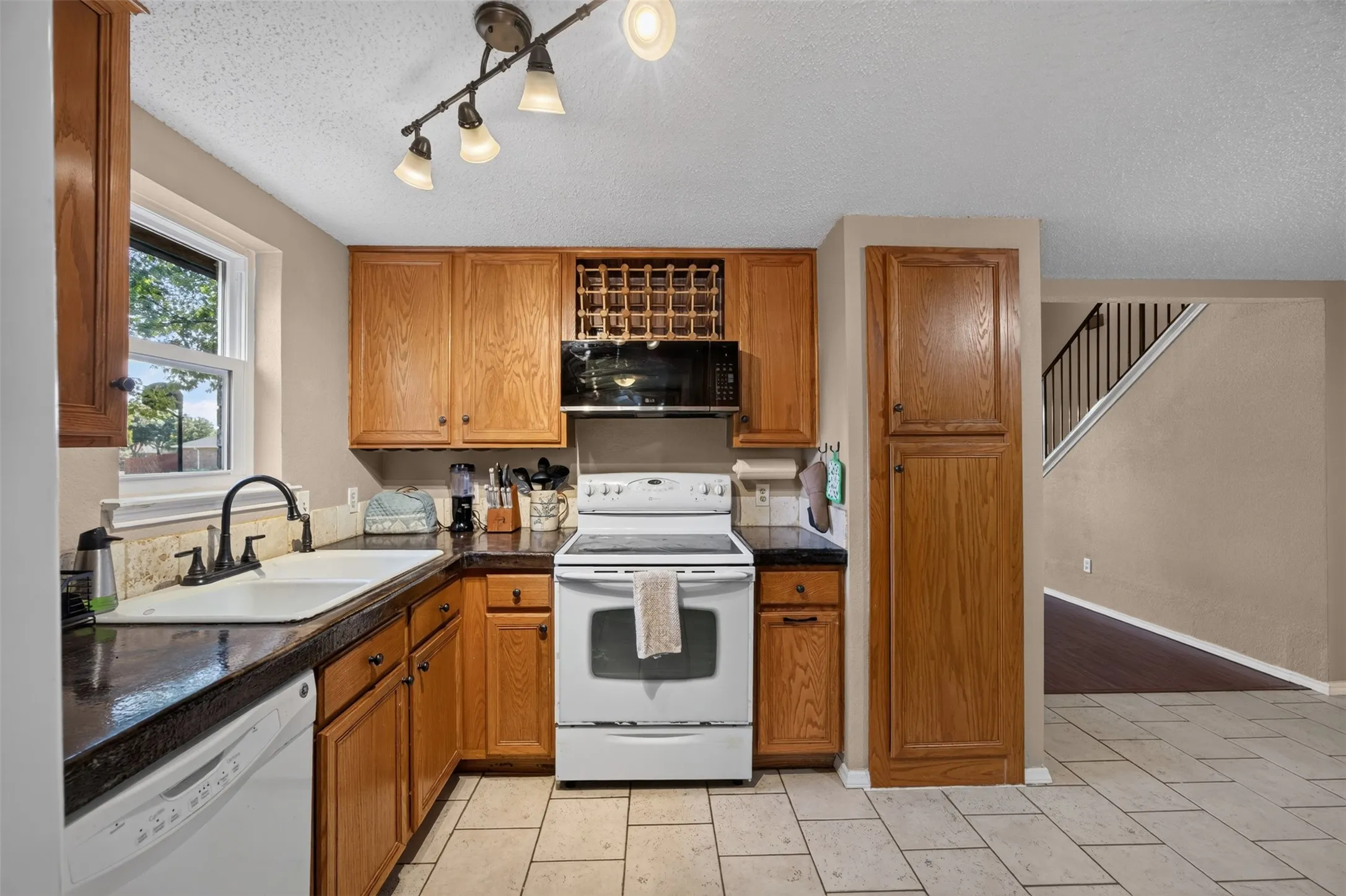 Kitchen featuring wood cabinetry, dark countertops, a built-in microwave, white appliances, and a tile floor