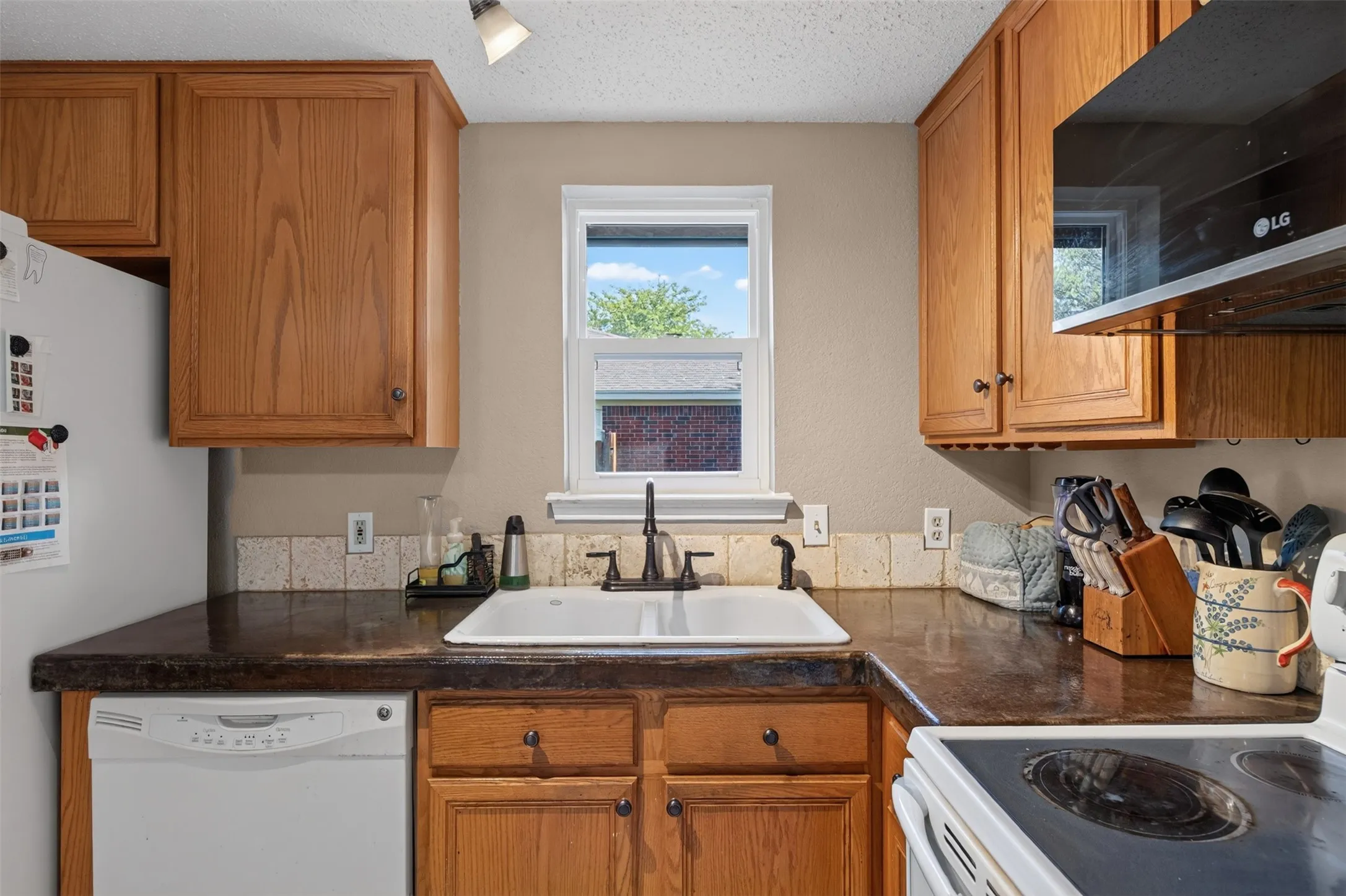 Warm wood cabinetry with dark countertops, a white undermount sink with a dark faucet, and a tiled backsplash