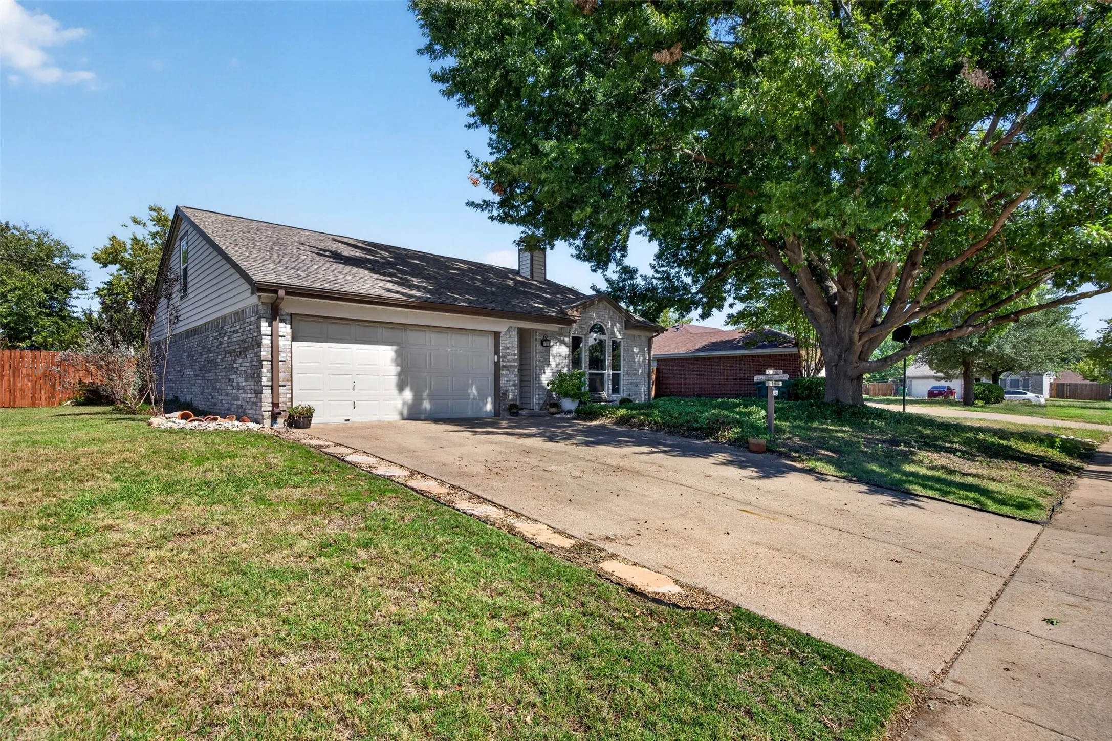 Exterior featuring a two-car garage, brick and siding facade, arched window with divided lites, mature tree, and concrete driveway