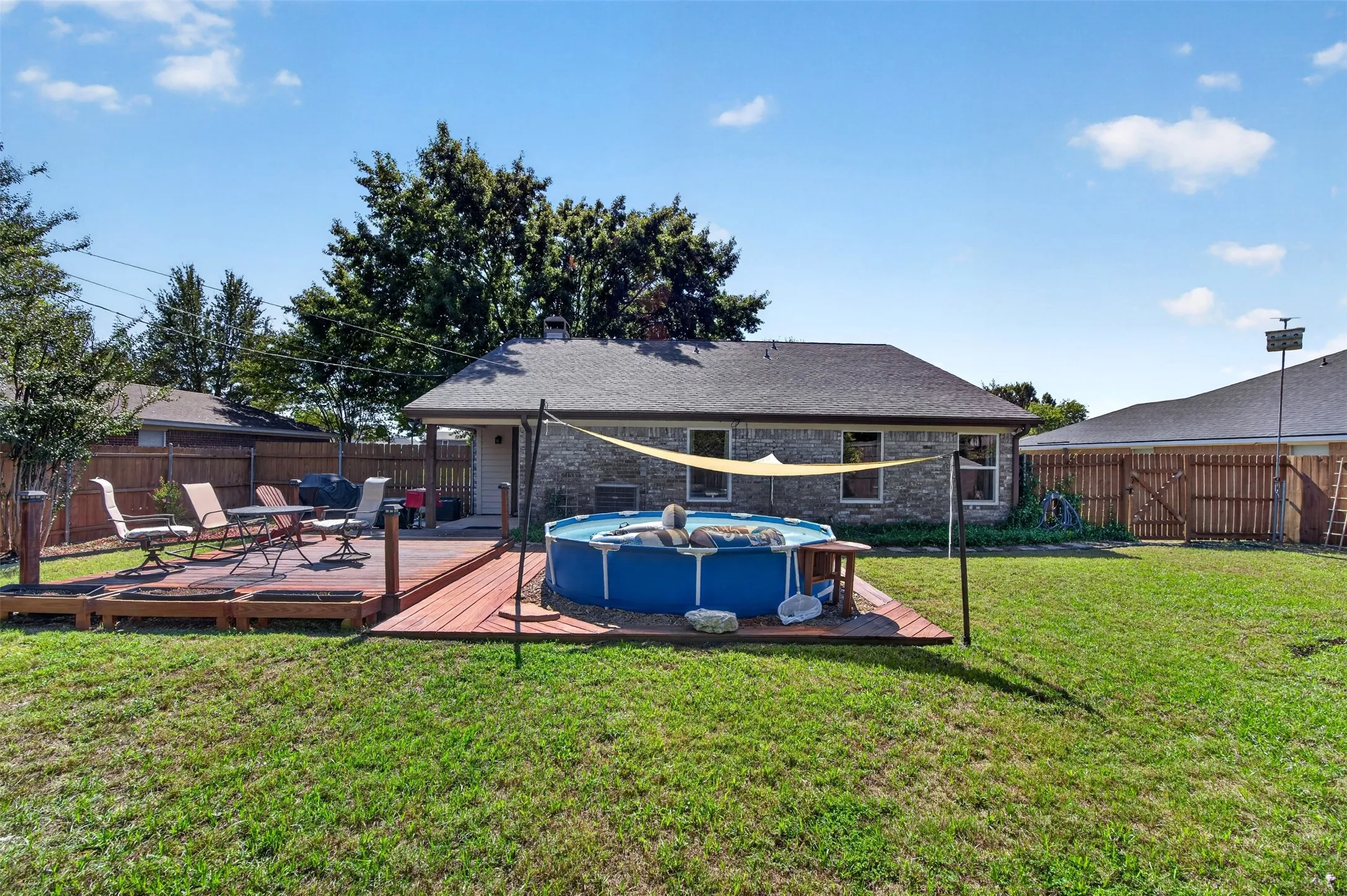 Expansive backyard featuring a wood deck with a built-in pool, a brick exterior, and a privacy fence