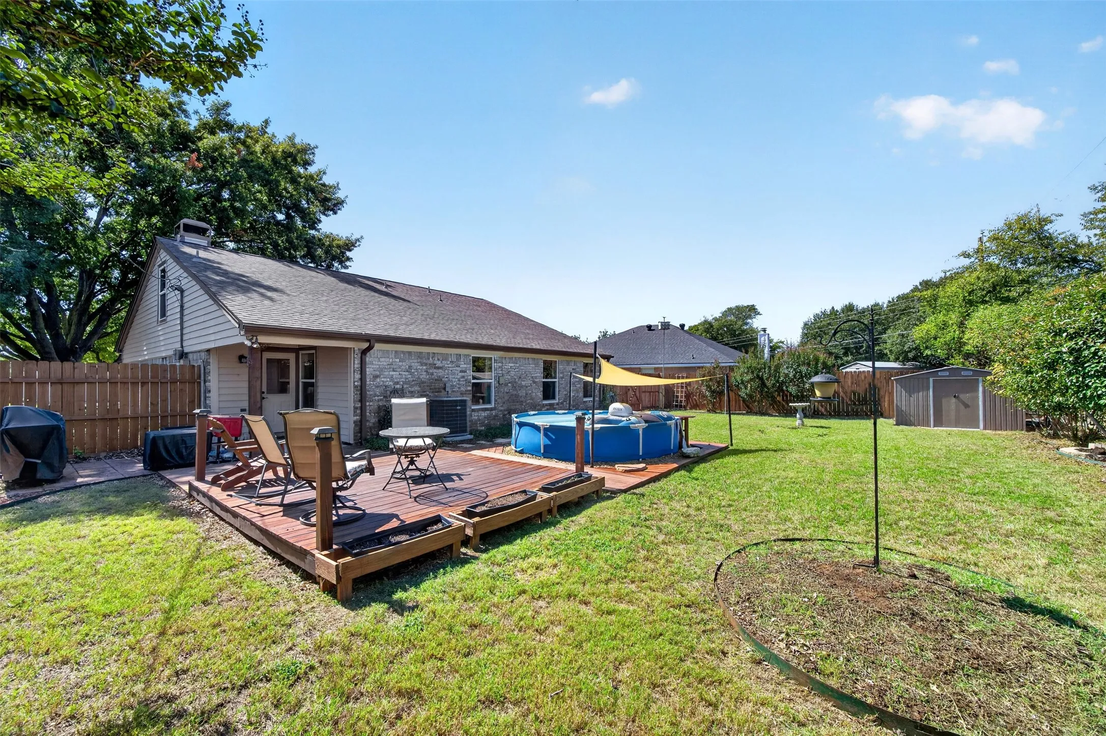 Expansive backyard featuring a wood deck, brick and siding exterior, fenced perimeter, and a storage shed