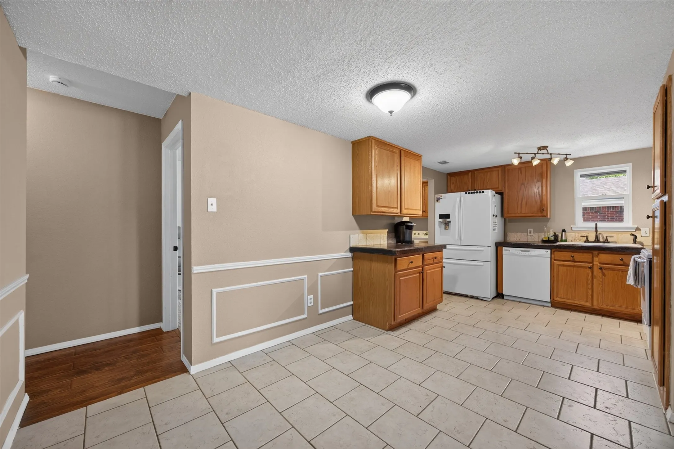 Kitchen with light wood-finish cabinetry, white appliances, and a tile backsplash