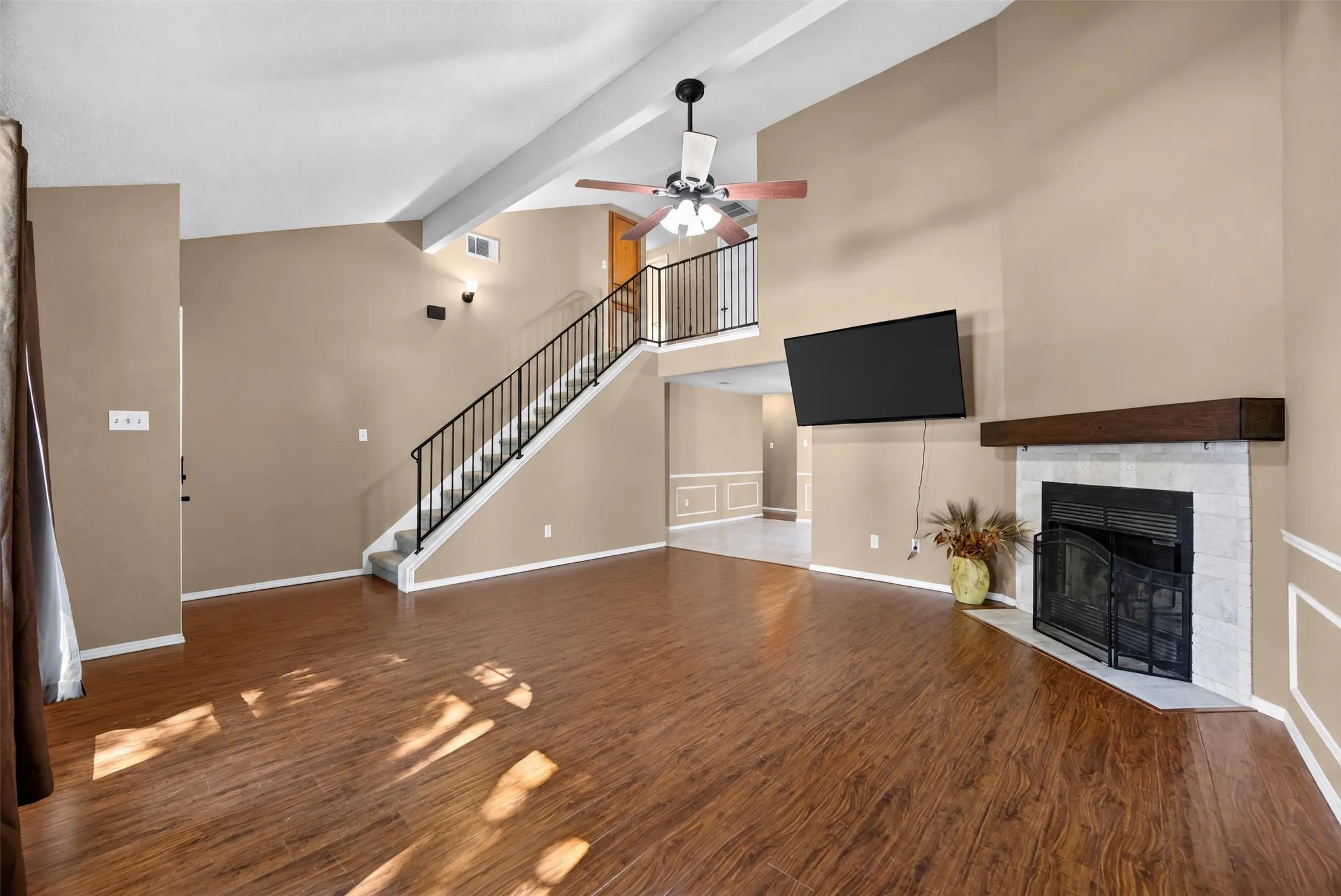 Vaulted ceiling with a ceiling fan, wood-finish flooring, fireplace with a tile surround and wood mantel, and a staircase with a black metal railing