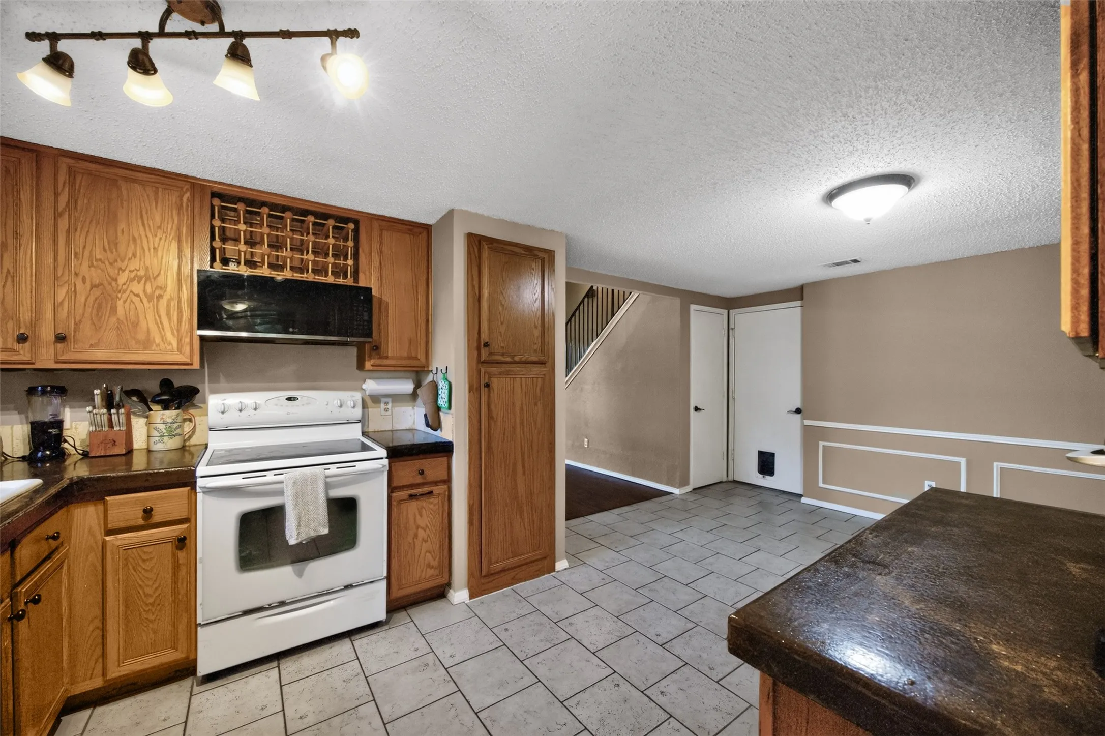 Kitchen featuring wood cabinetry, built-in wine rack, tile flooring, and integrated white appliances