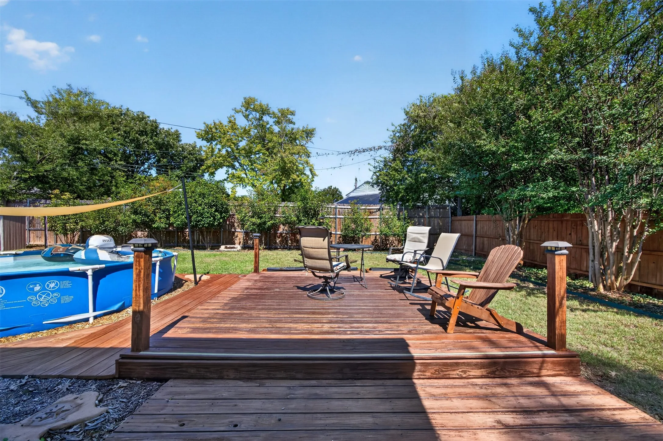 Expansive backyard featuring a wood-finish deck with integrated lighting, a manicured lawn, and mature trees