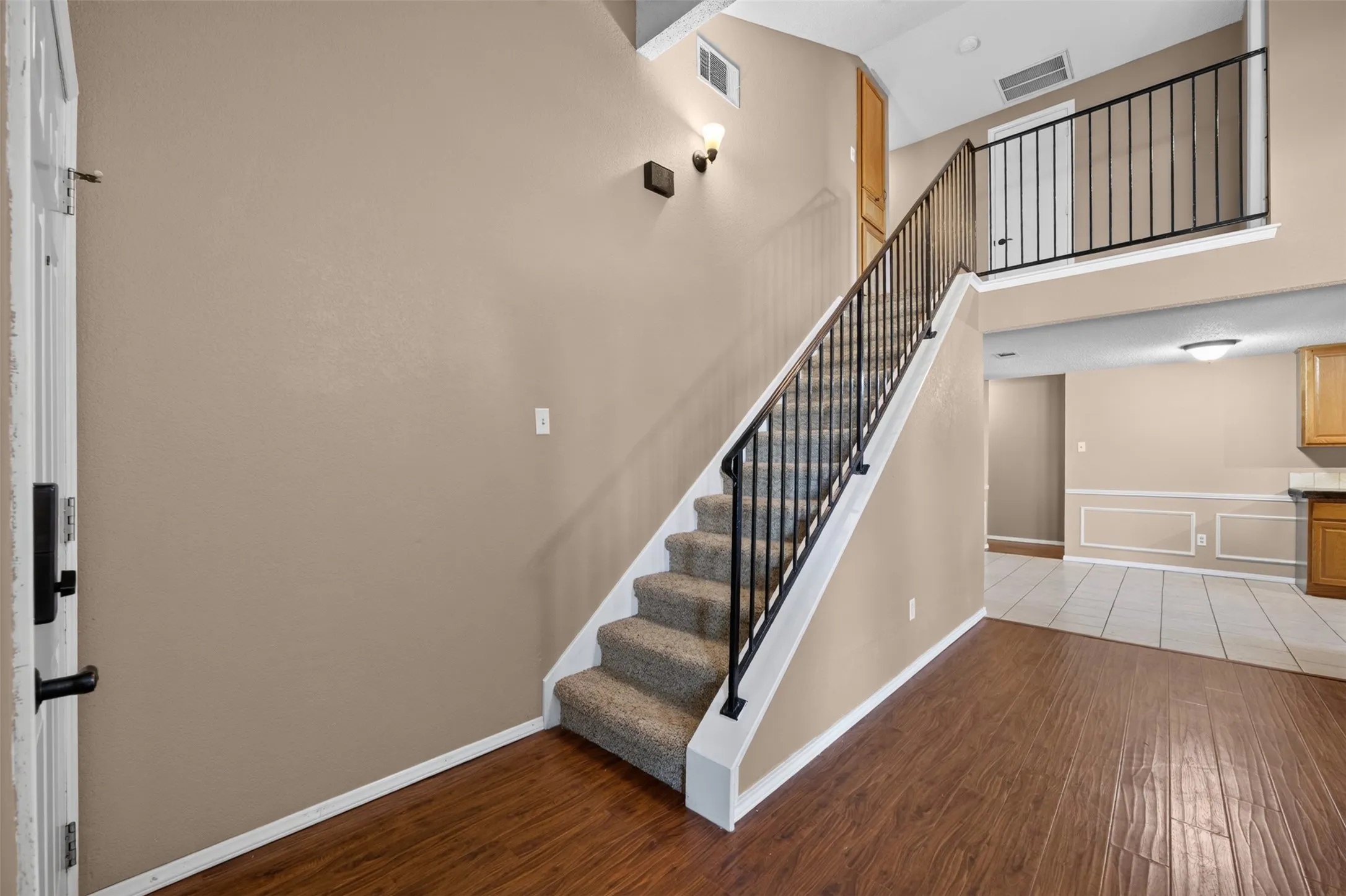 Two-story entry with wood-finish flooring, carpeted staircase, wrought iron railing, and neutral wall tones