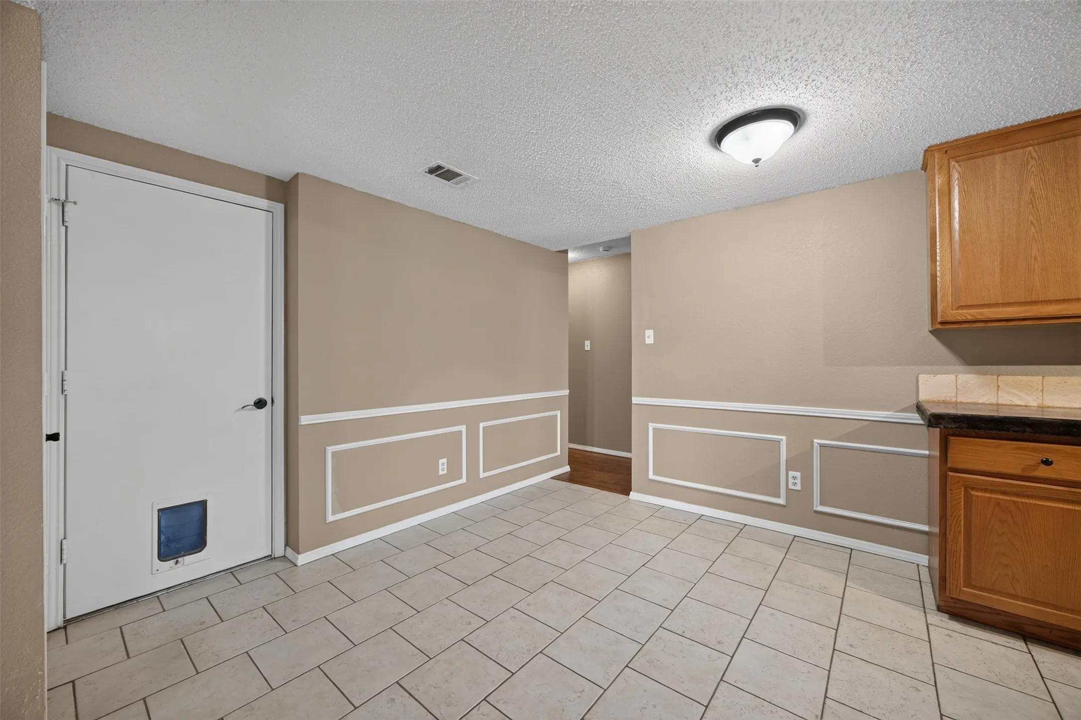 Tile flooring, wainscoting, wood cabinetry, stone-look countertop, and a tiled backsplash
