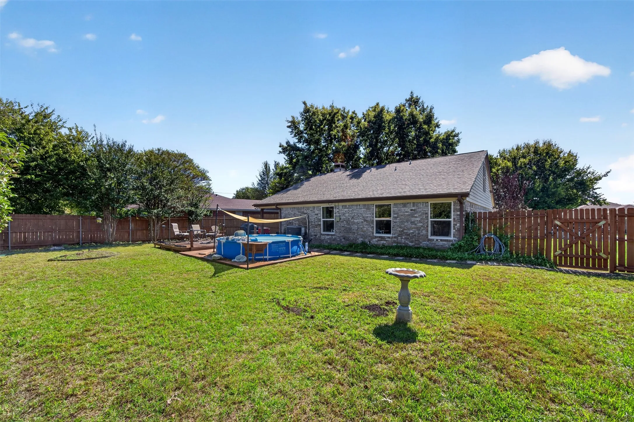 Expansive backyard featuring a large grass area, wood privacy fencing, and a raised wood deck with an above-ground pool