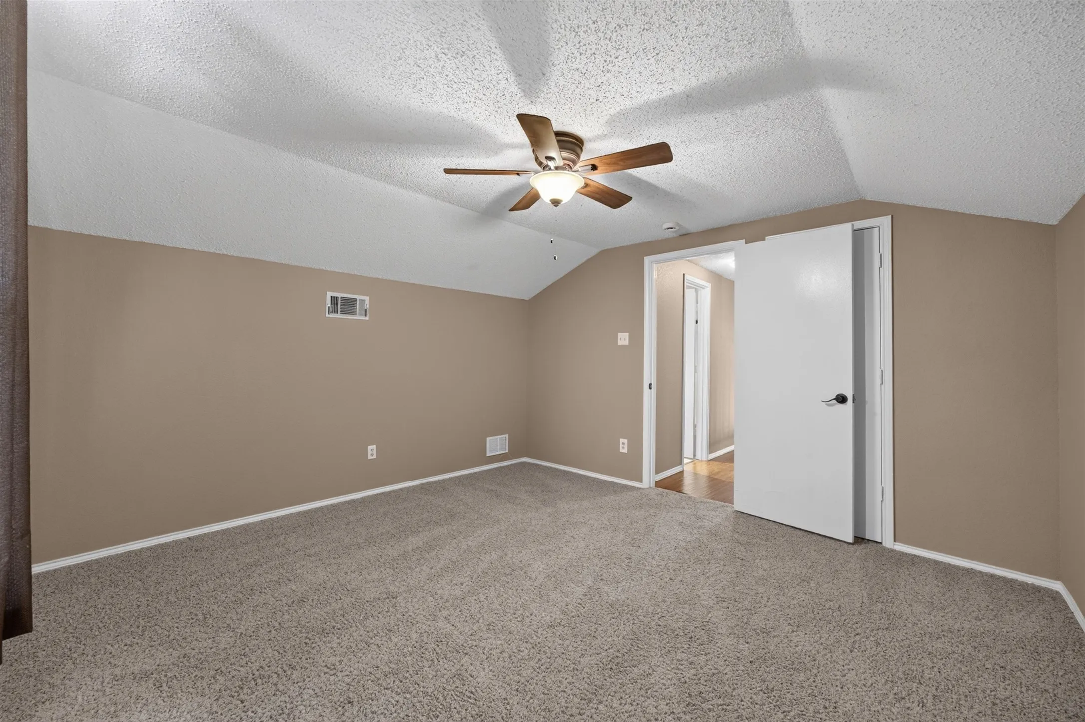 Carpeted room with a ceiling fan, sloped ceilings, and a light-colored door