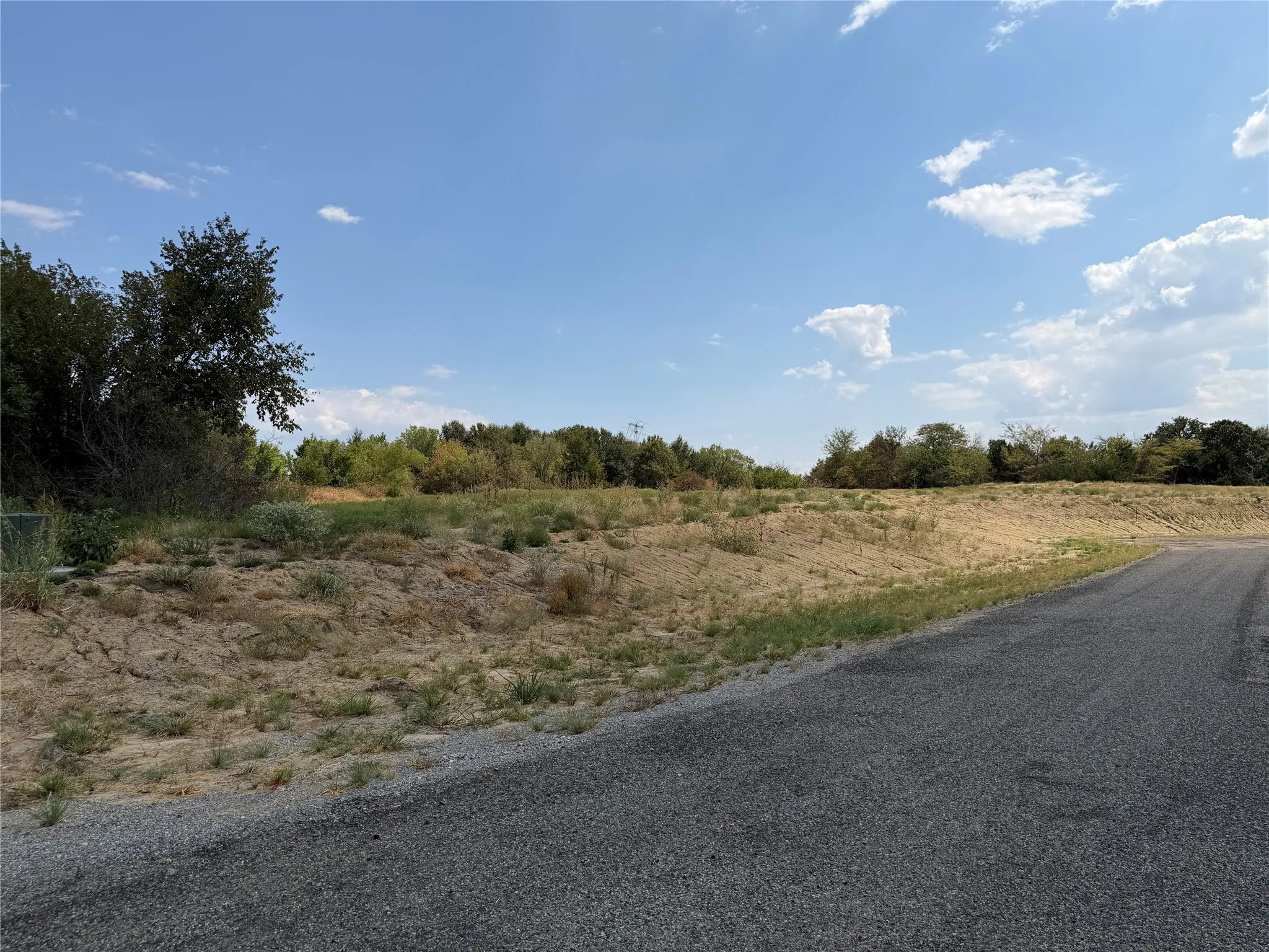 Paved road frontage, elevated terrain, and distant tree line