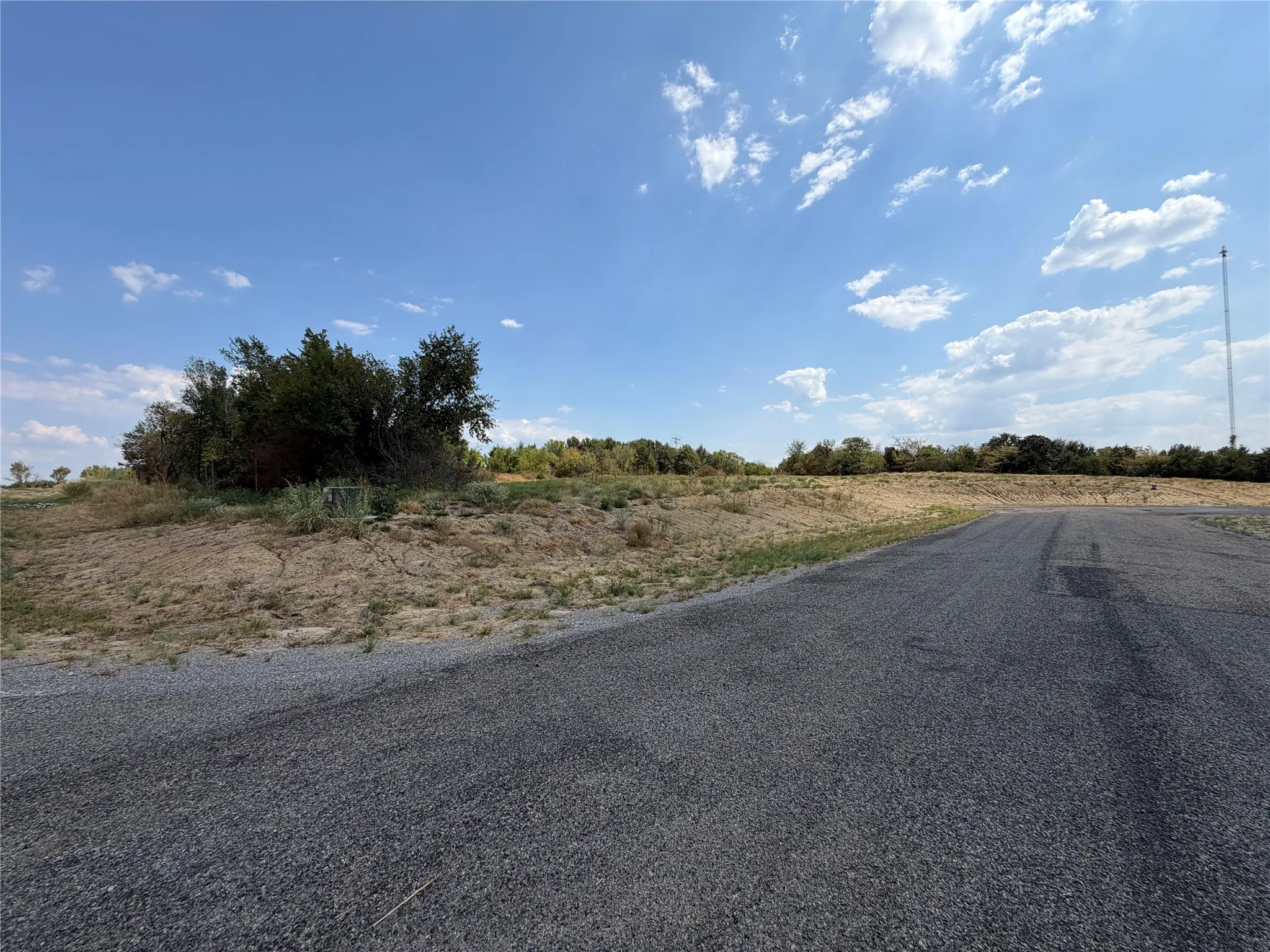 Expansive undeveloped land featuring a paved road, mature trees, and varied topography