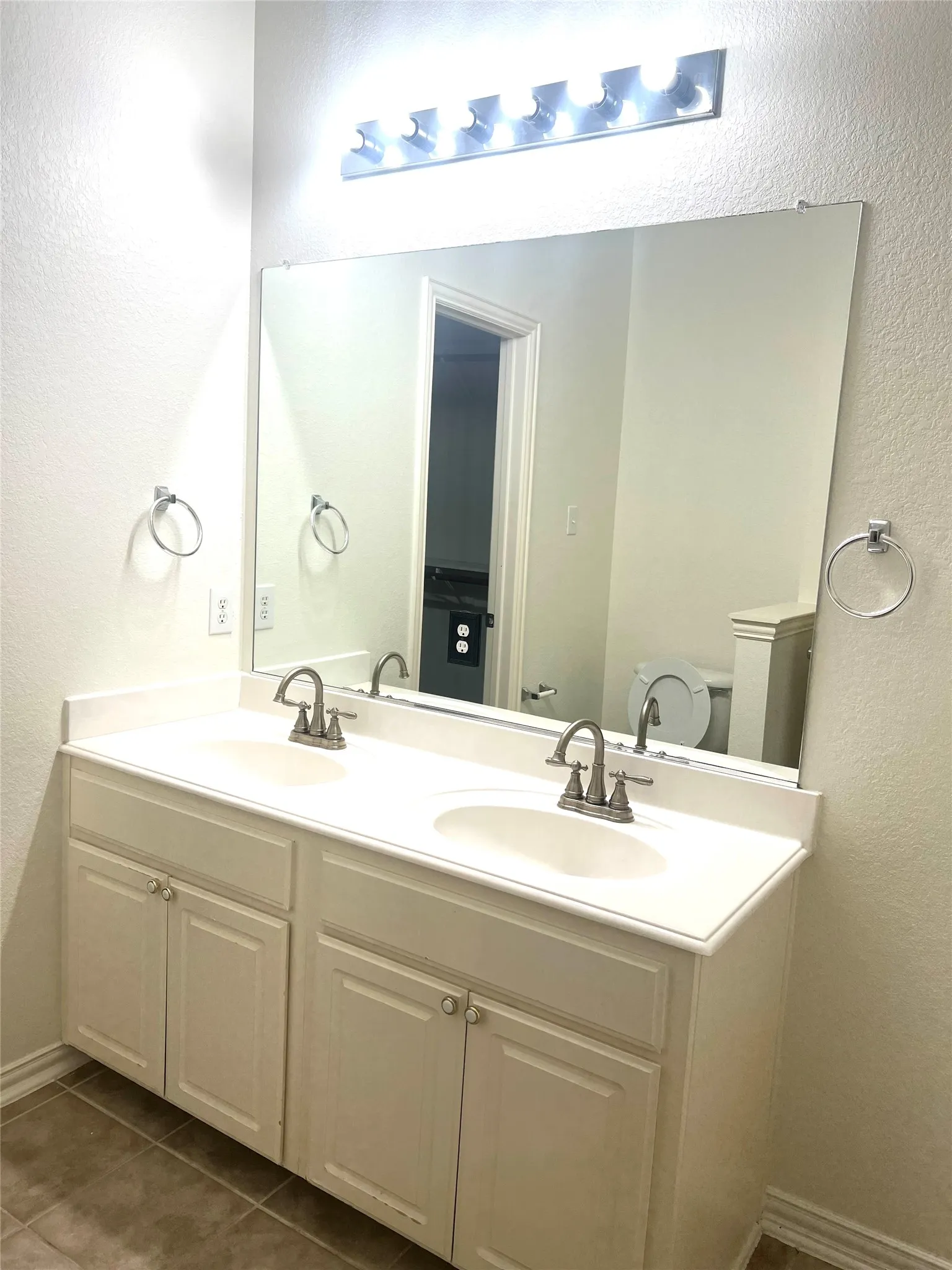Bathroom featuring a textured wall, double vanity, and dark tile patterned floors