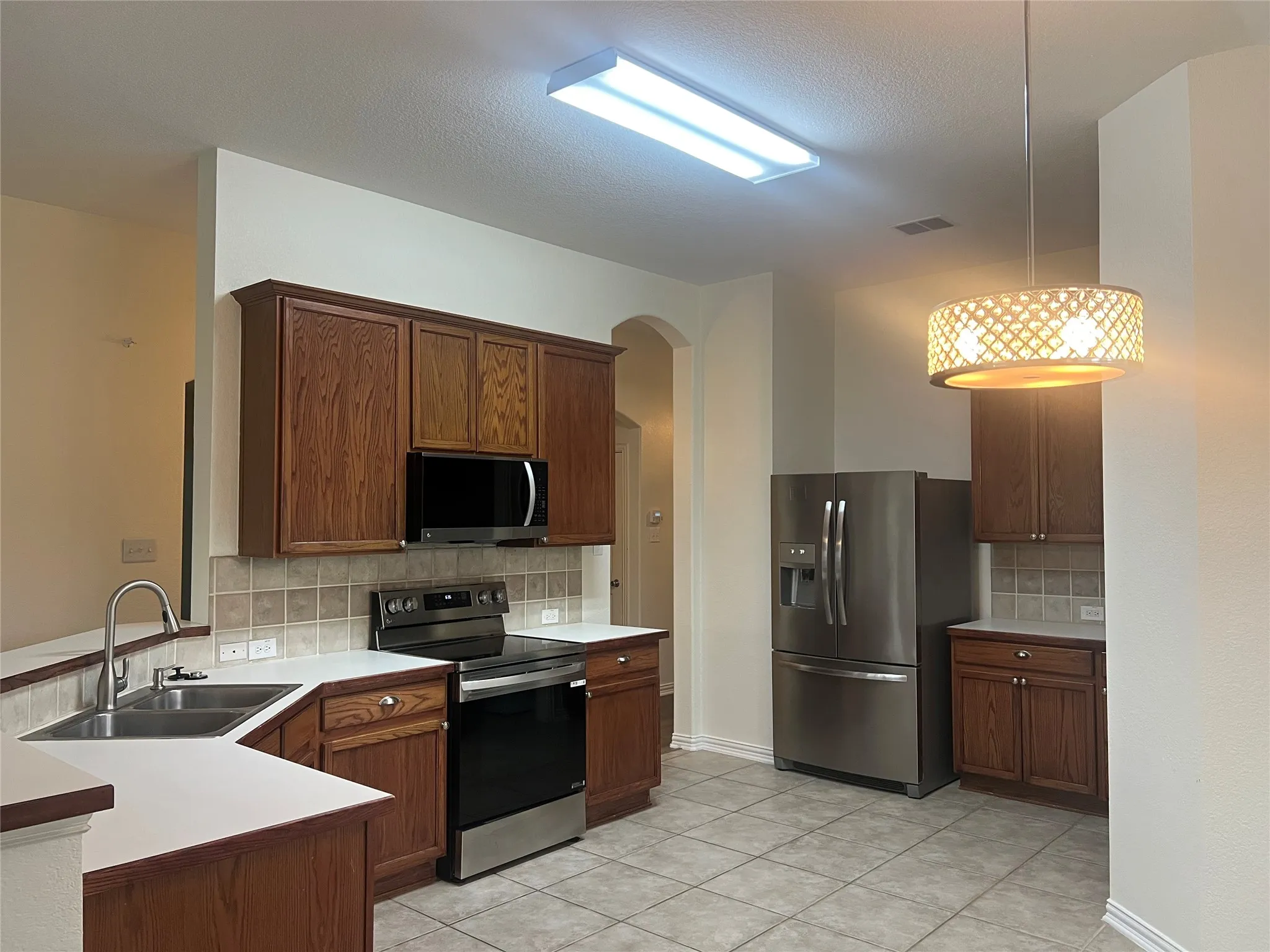 Kitchen featuring stainless steel appliances, backsplash, light countertops, arched walkways, and light tile patterned flooring