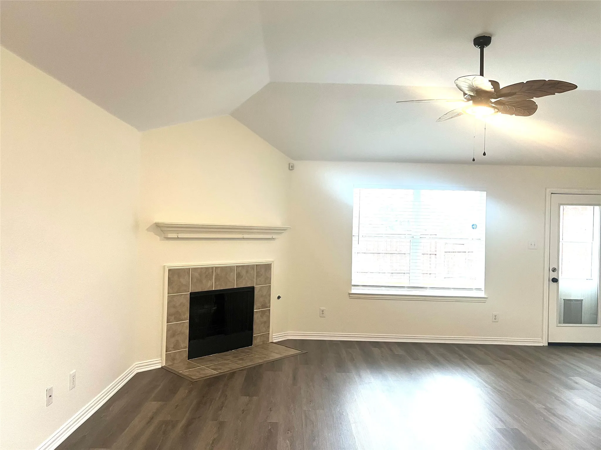 Unfurnished living room featuring dark wood-style flooring, a tile fireplace, ceiling fan, and vaulted ceiling