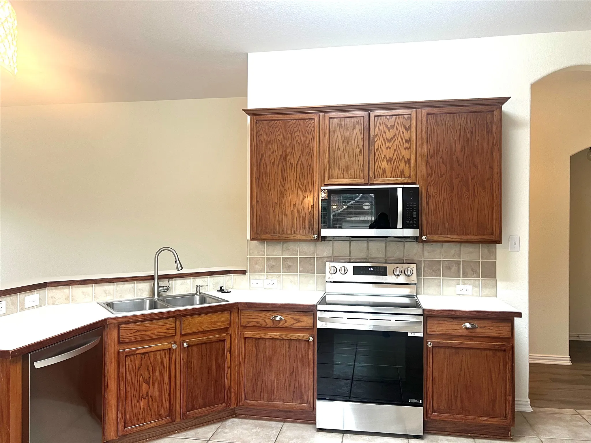 Kitchen featuring appliances with stainless steel finishes, arched walkways, decorative backsplash, and light countertops