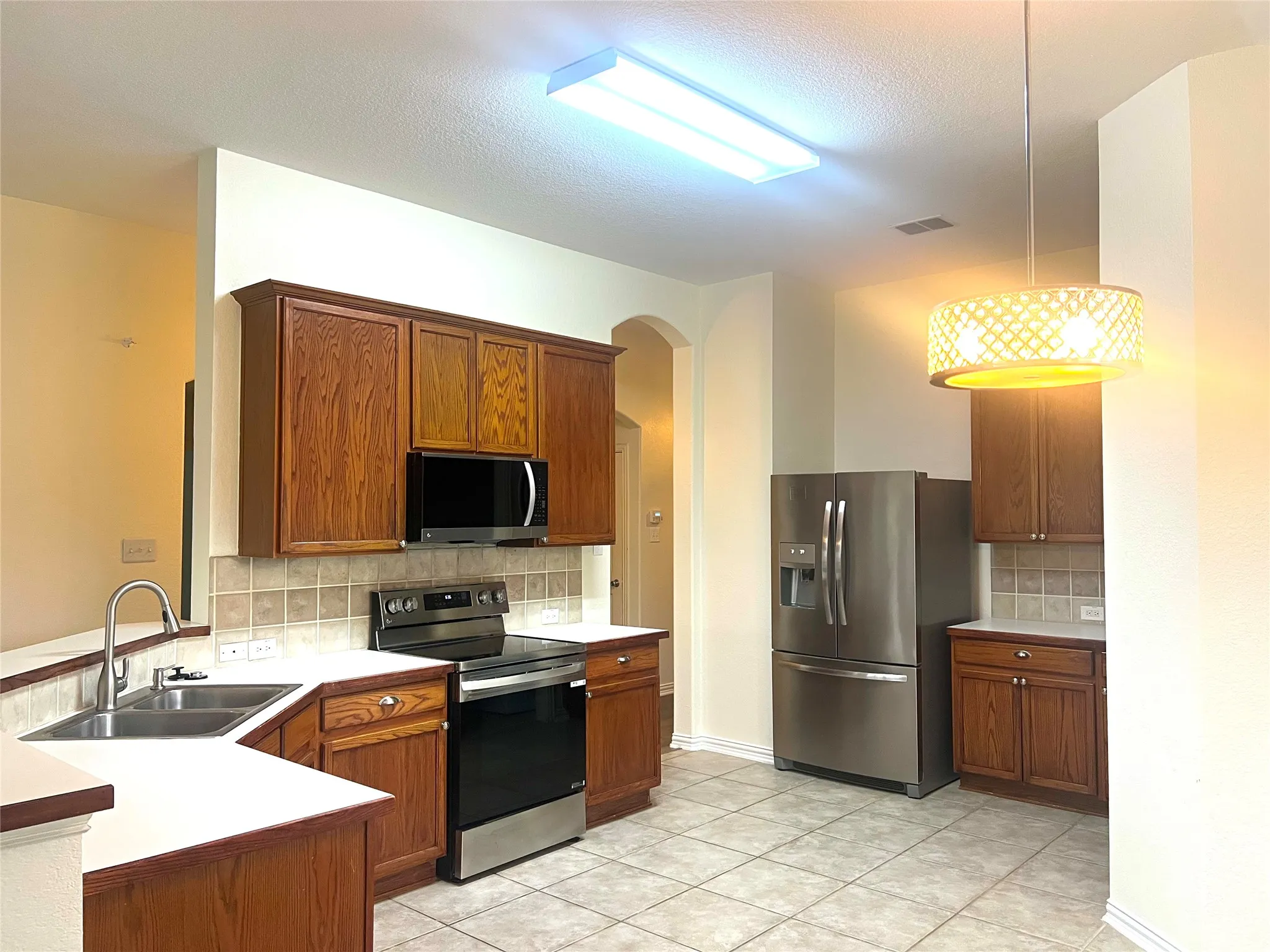 Kitchen featuring stainless steel appliances, tasteful backsplash, brown cabinets, light countertops, and a textured ceiling