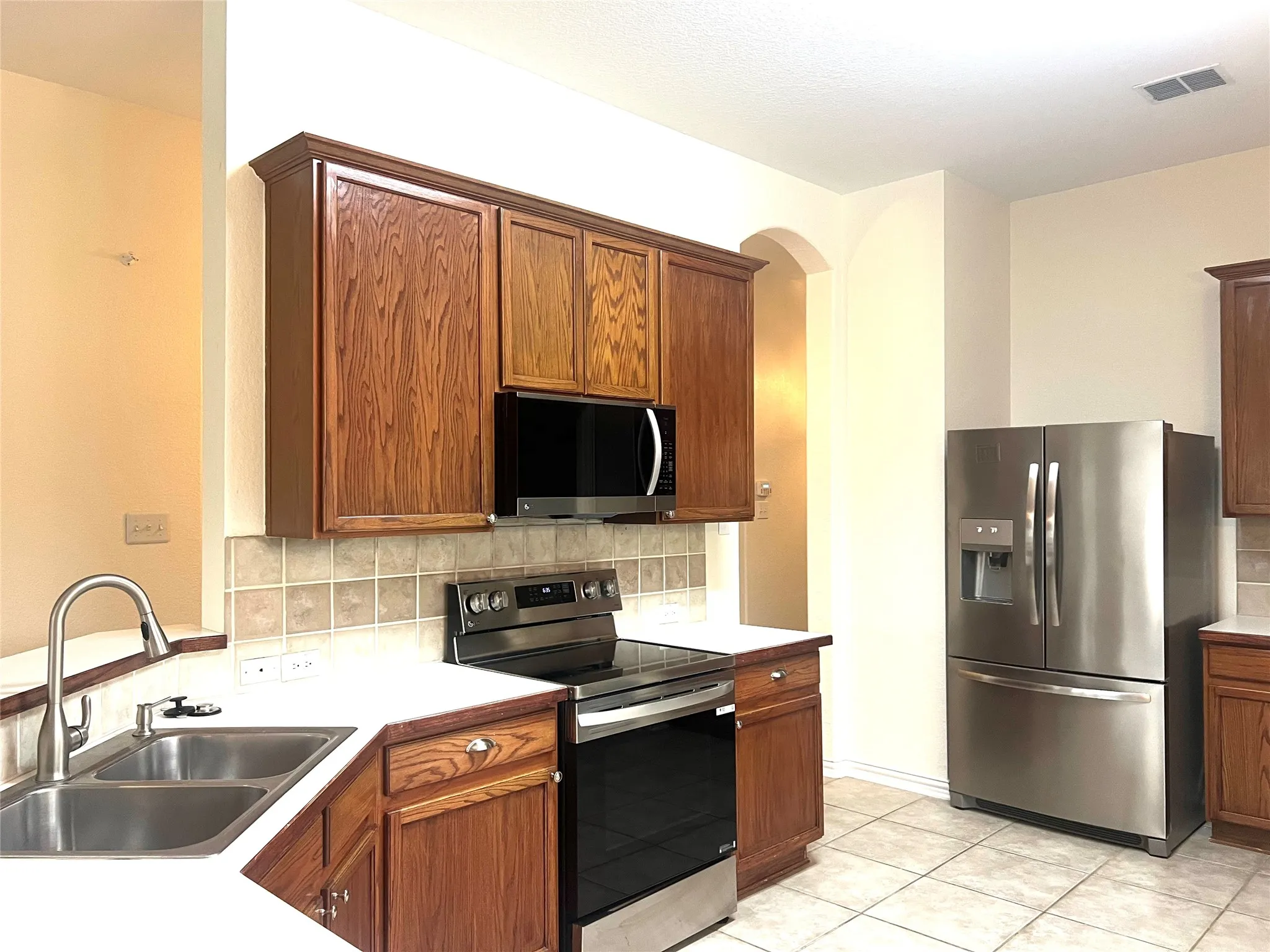 Kitchen featuring tasteful backsplash, stainless steel appliances, light countertops, brown cabinetry, and light tile patterned floors