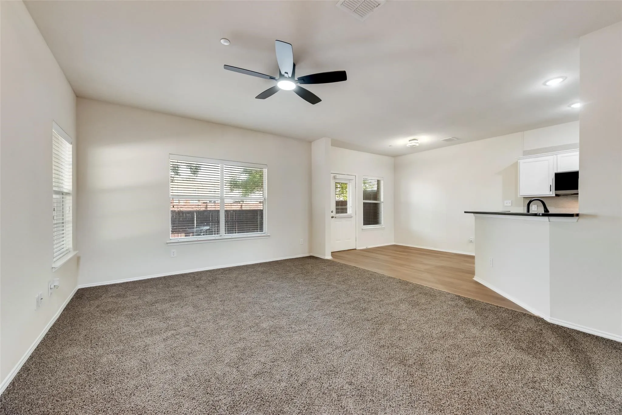 Vaulted ceilings with a ceiling fan, dual windows with blinds, wood-finish flooring, and white cabinetry