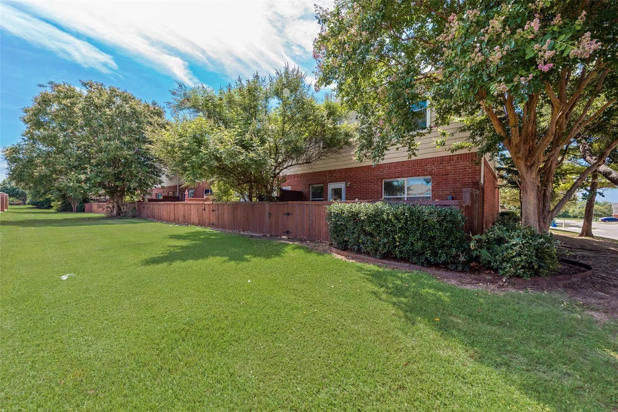 Expansive lawn area with mature trees, established shrubbery, and a wood privacy fence