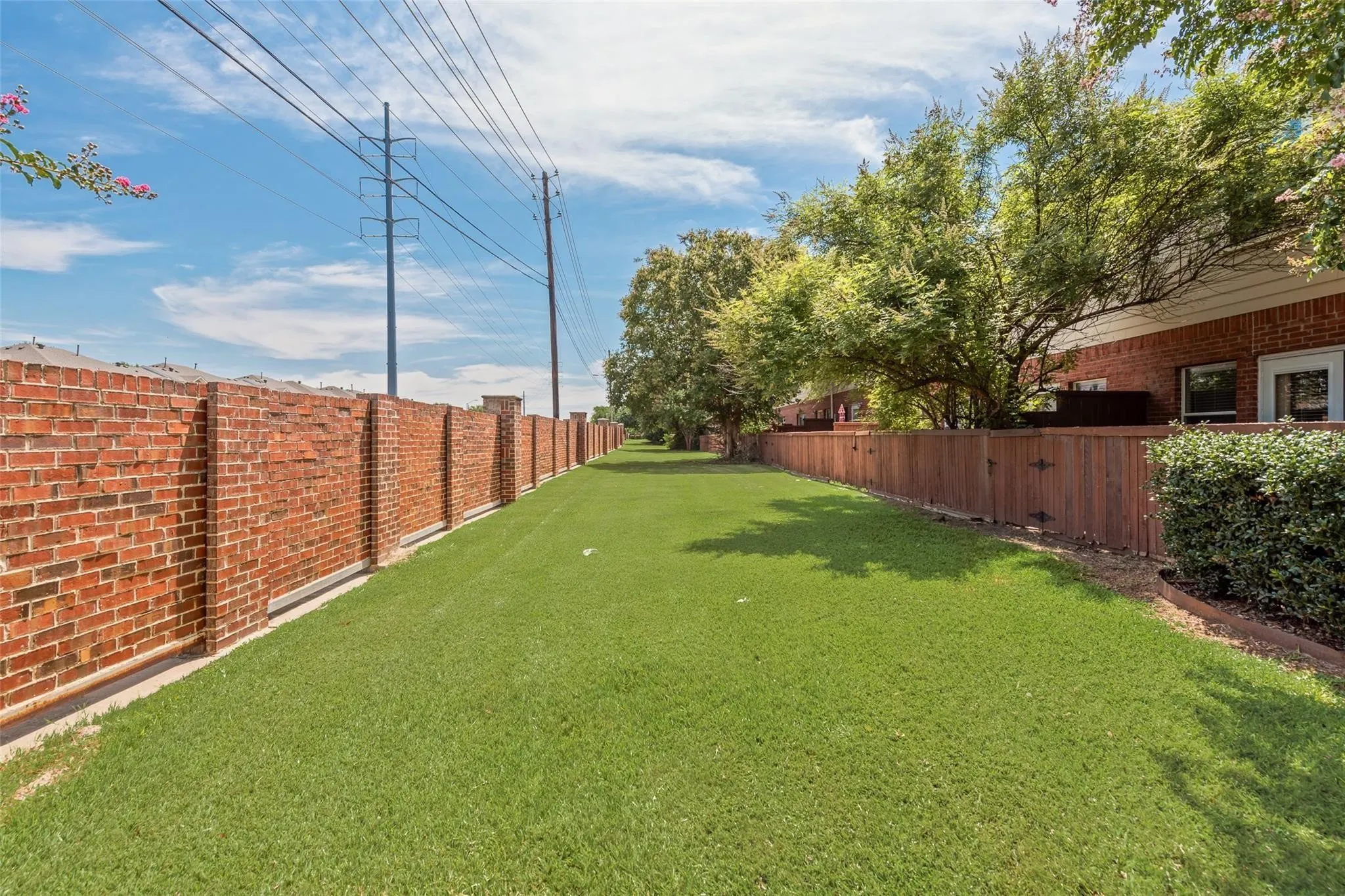 Expansive green space featuring a brick privacy wall, wood fence, and mature trees