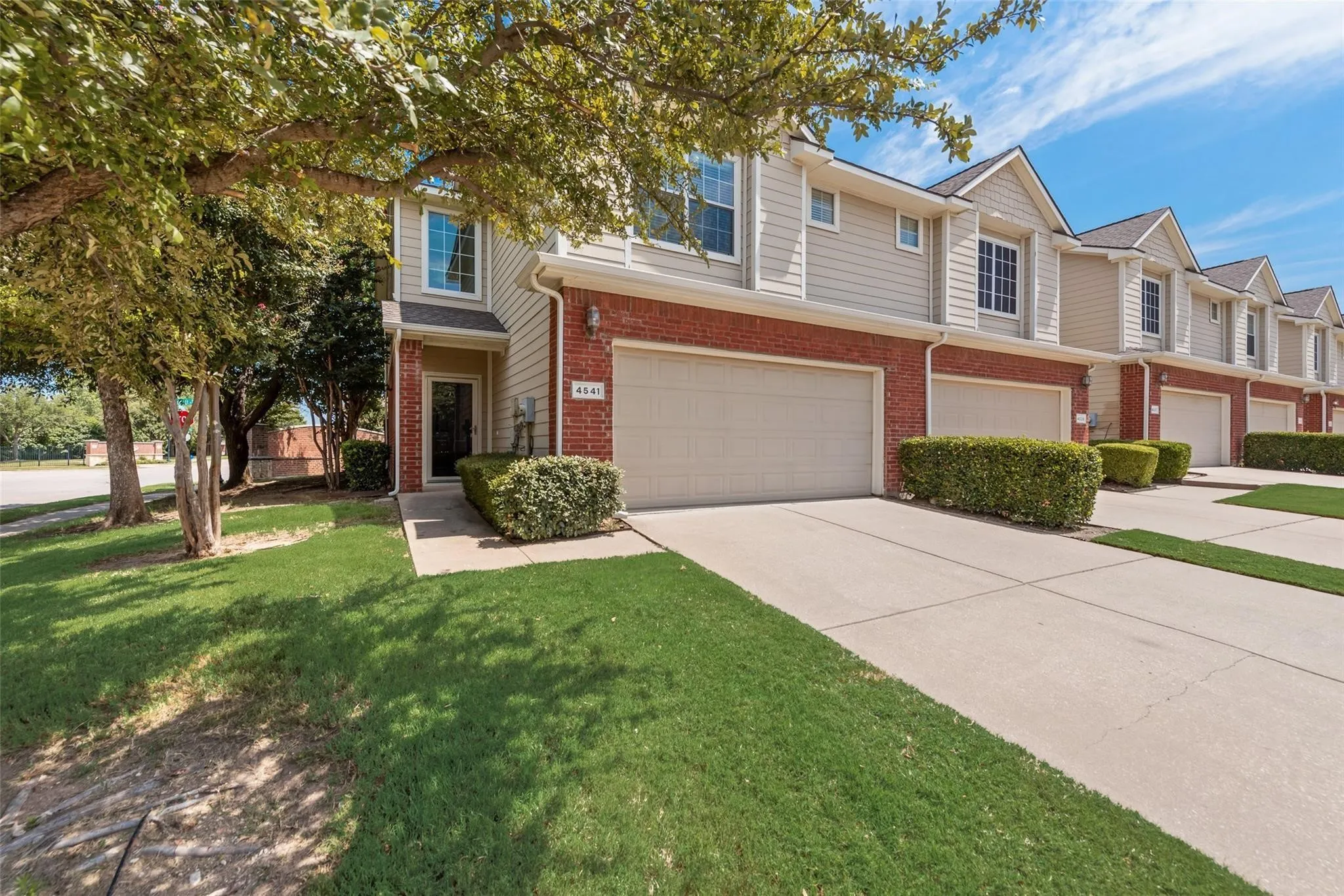 Brick and siding exterior with a pitched roofline, attached garage, concrete driveway, and manicured landscaping