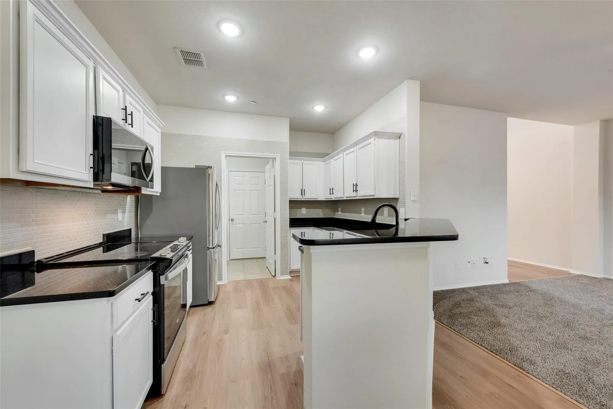 Kitchen featuring white cabinetry, dark countertops, stainless steel appliances, wood-finish flooring, and recessed lighting