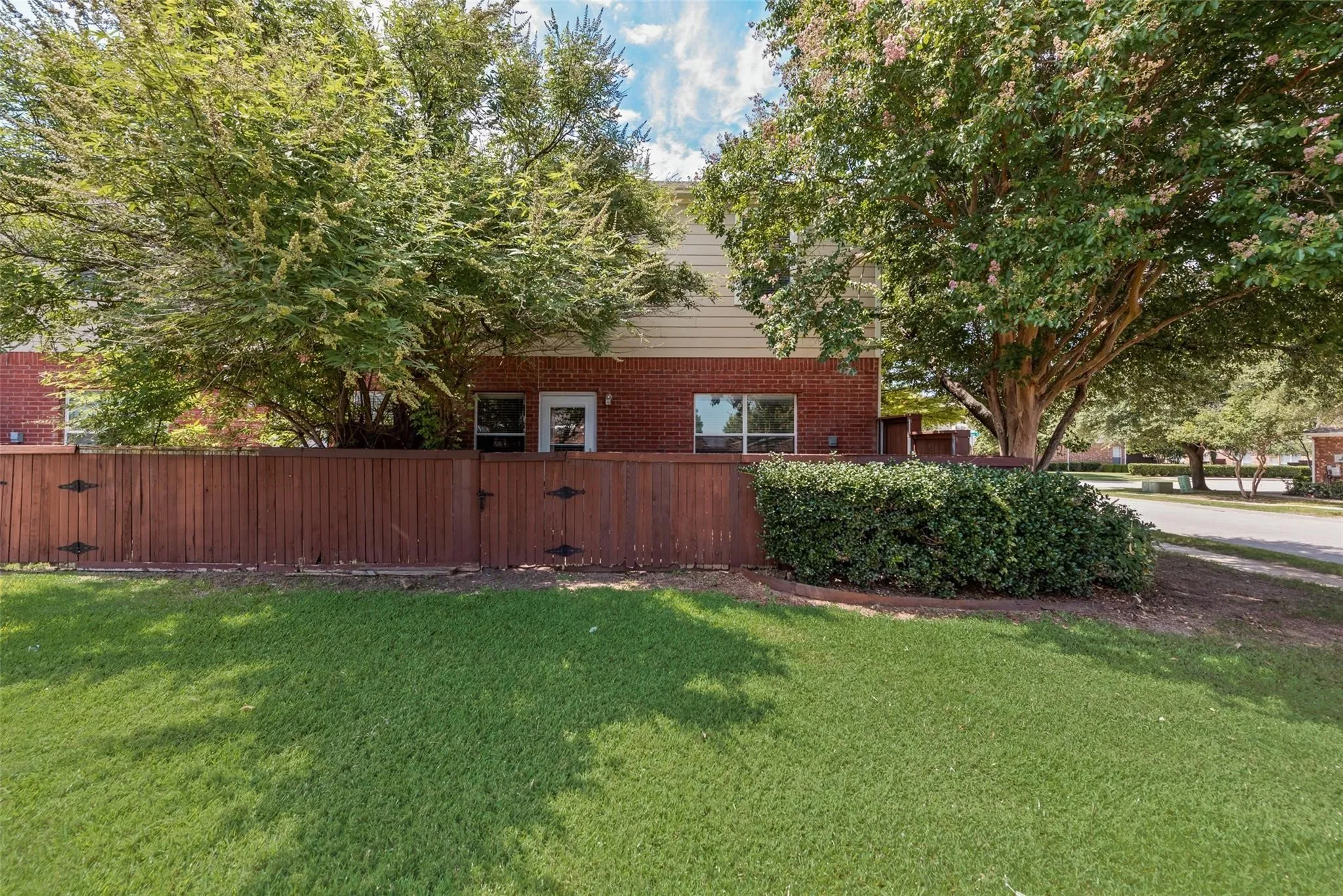 Private fenced yard with lush green lawn, mature trees, and brick exterior
