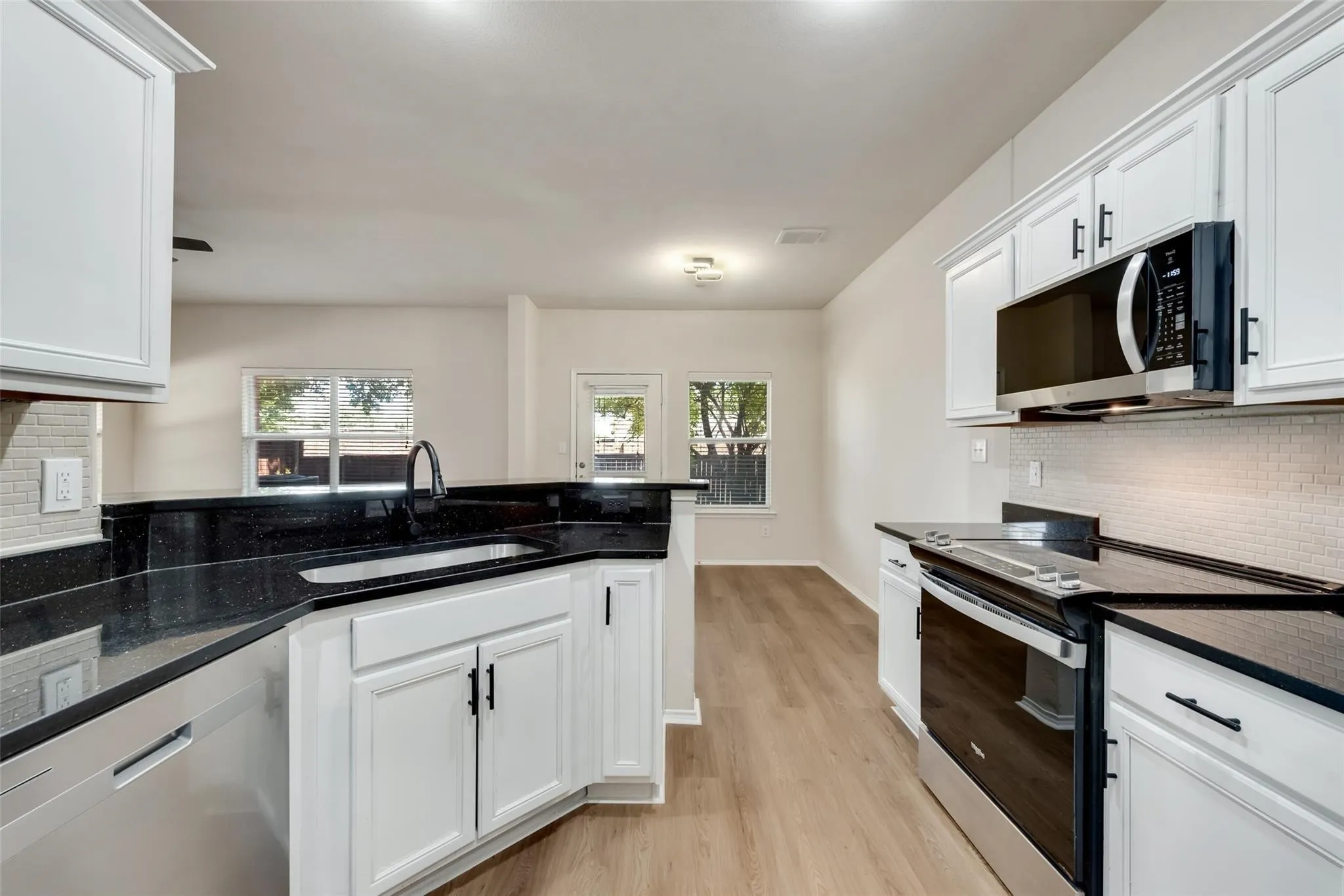 Kitchen featuring dark countertops, white cabinetry with dark hardware, stainless steel appliances, and a tile backsplash