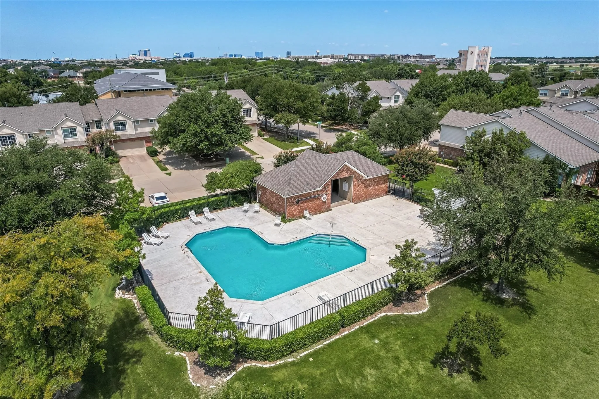 Community swimming pool with surrounding concrete decking, brick pool house, and perimeter fencing