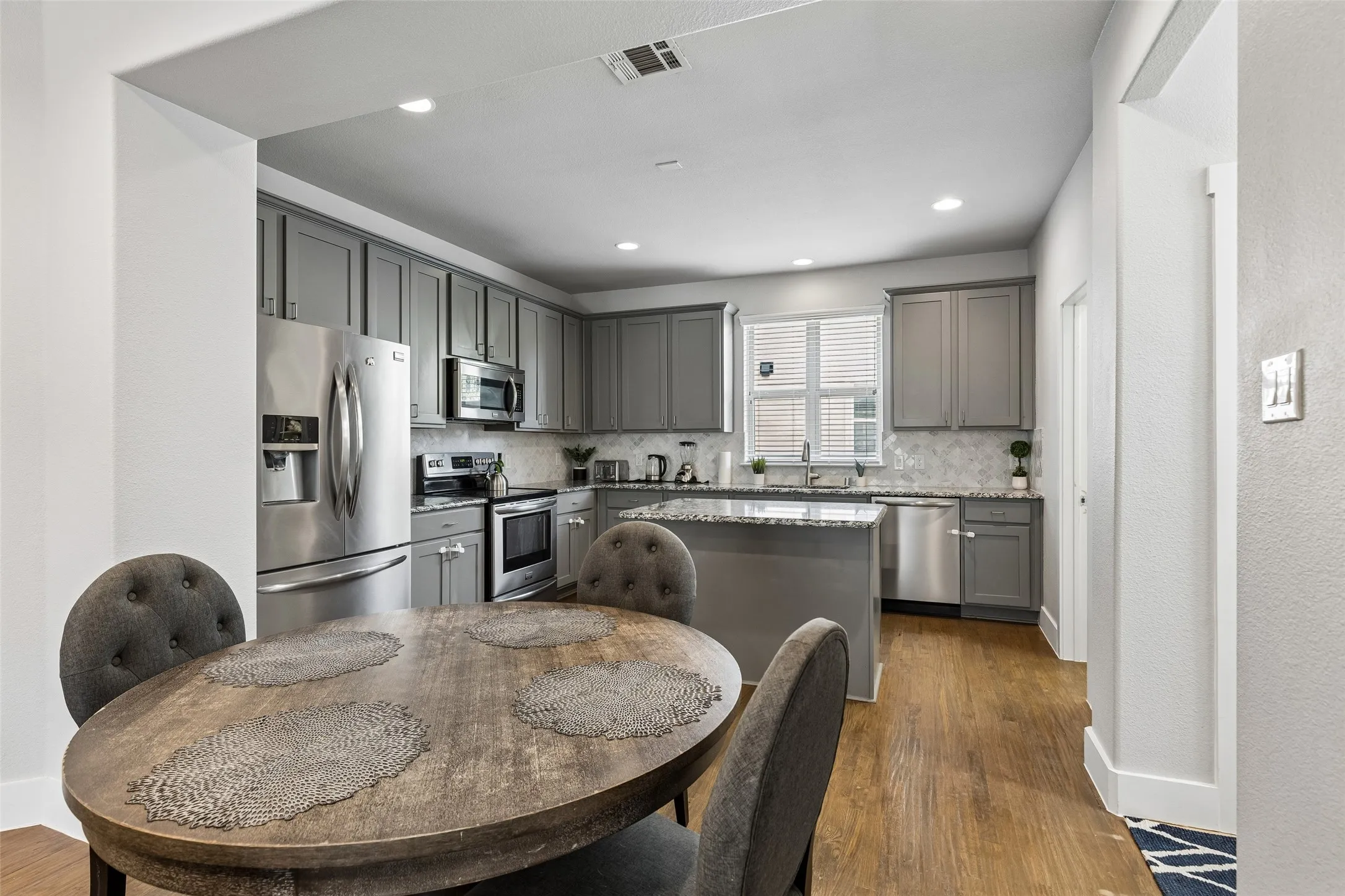 Kitchen featuring stainless steel appliances, grey shaker-style cabinetry, a central island with countertop, and wood-finish flooring