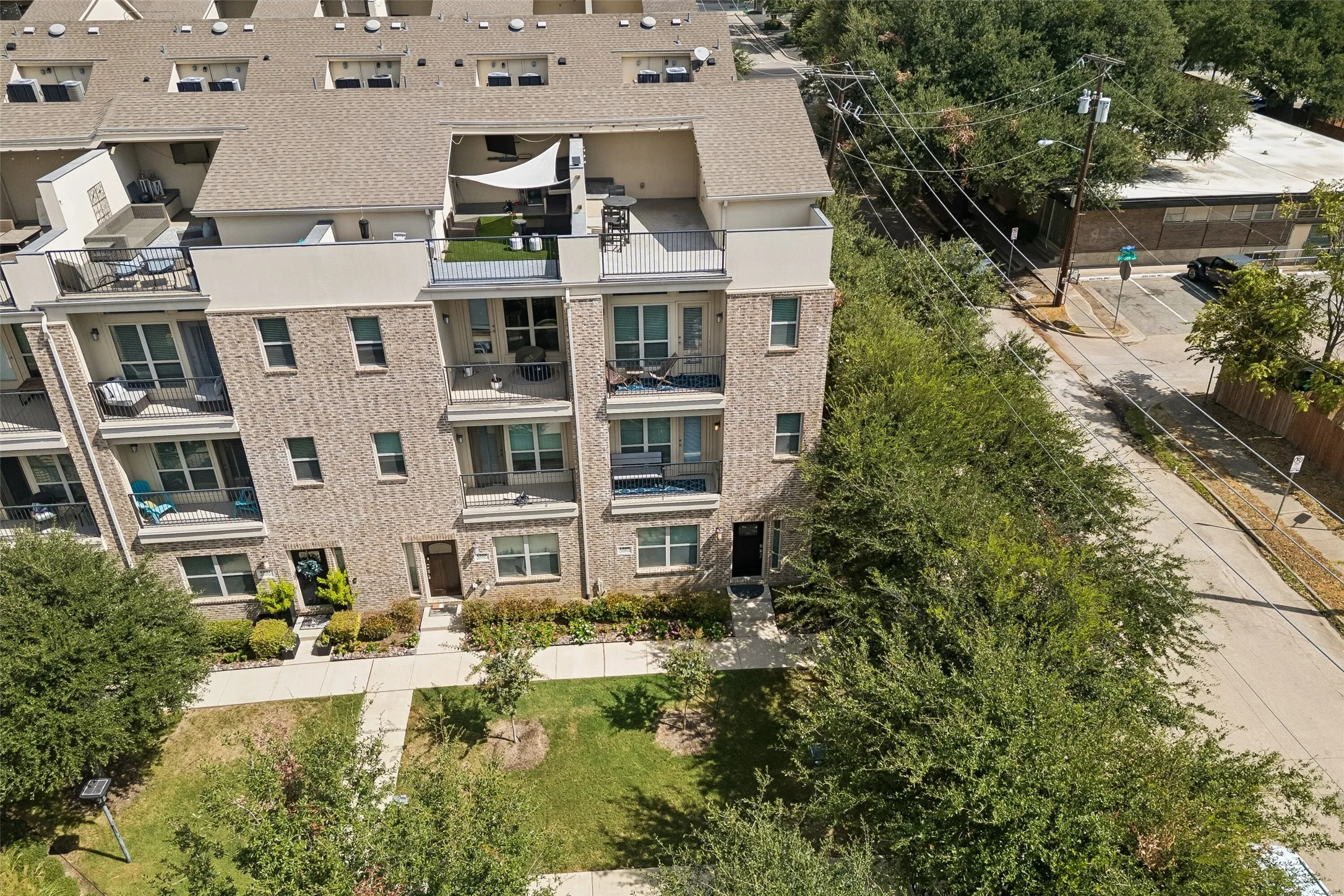 Multi-story townhome featuring brick and stucco exterior, multiple private balconies, and a rooftop terrace with artificial turf