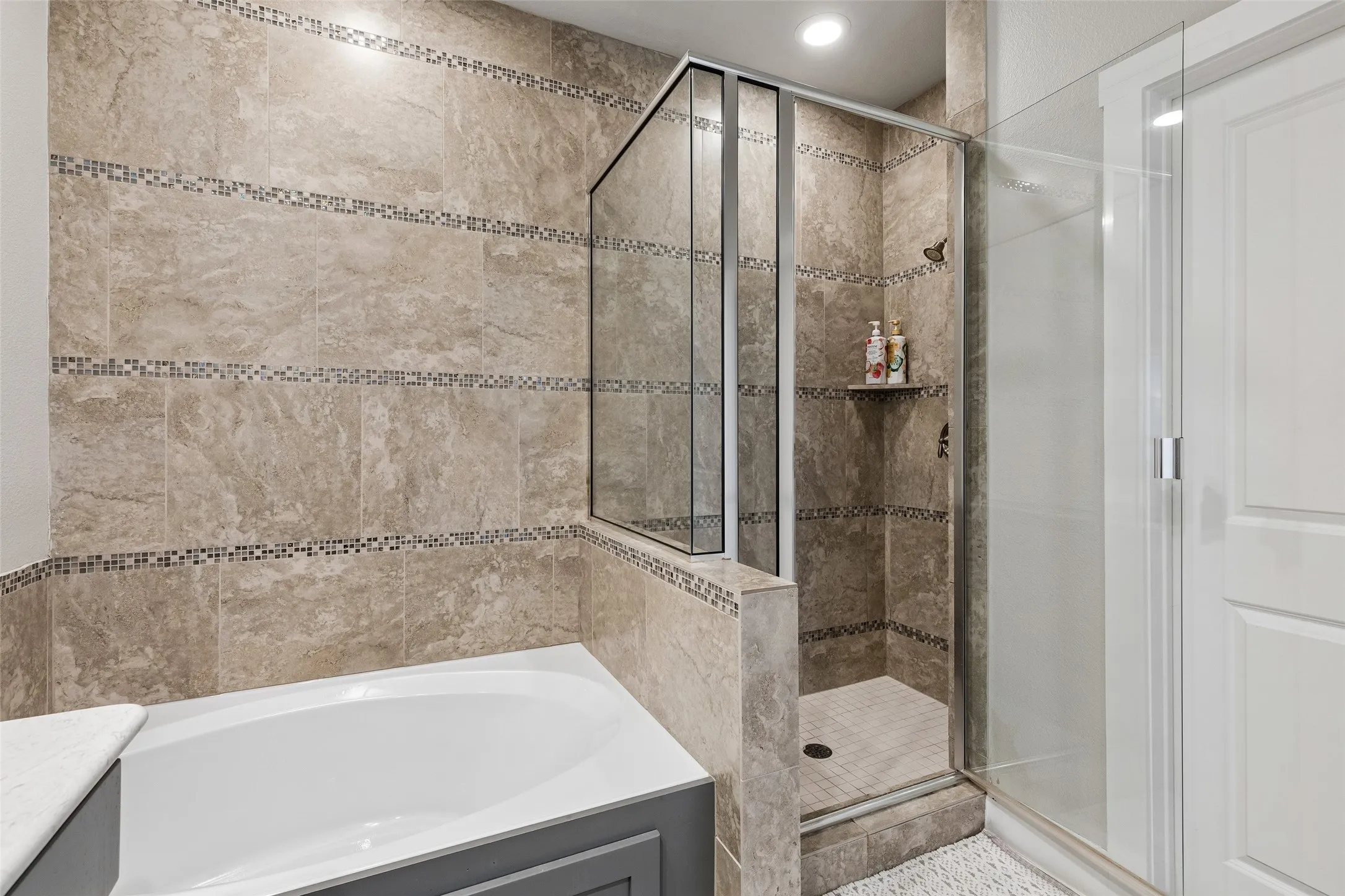 Tiled shower enclosure with built-in shelf, glass shower door, and coordinated tile bathtub surround with mosaic accents