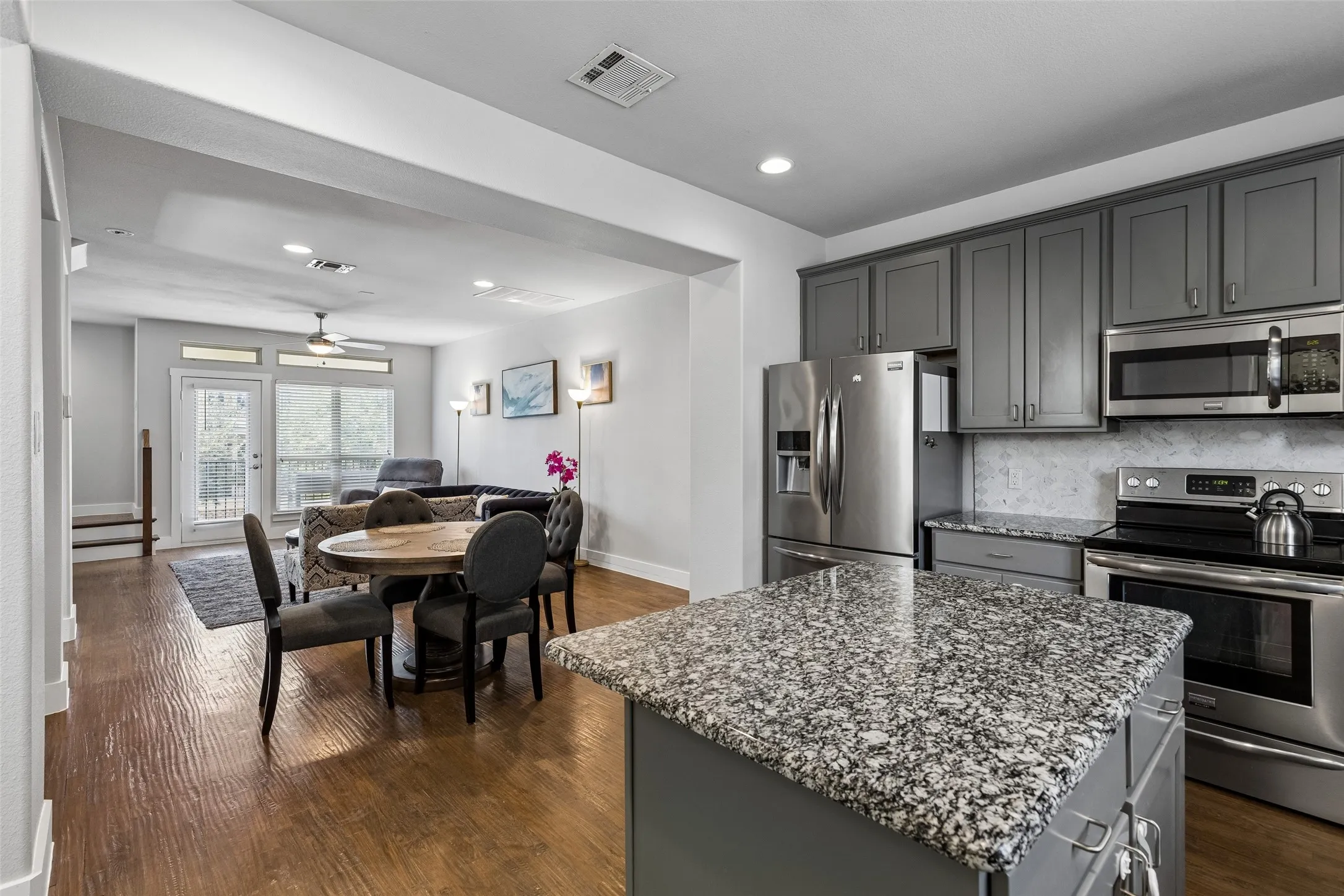 Kitchen featuring gray cabinetry, stainless steel appliances, speckled stone countertops, and a tile backsplash