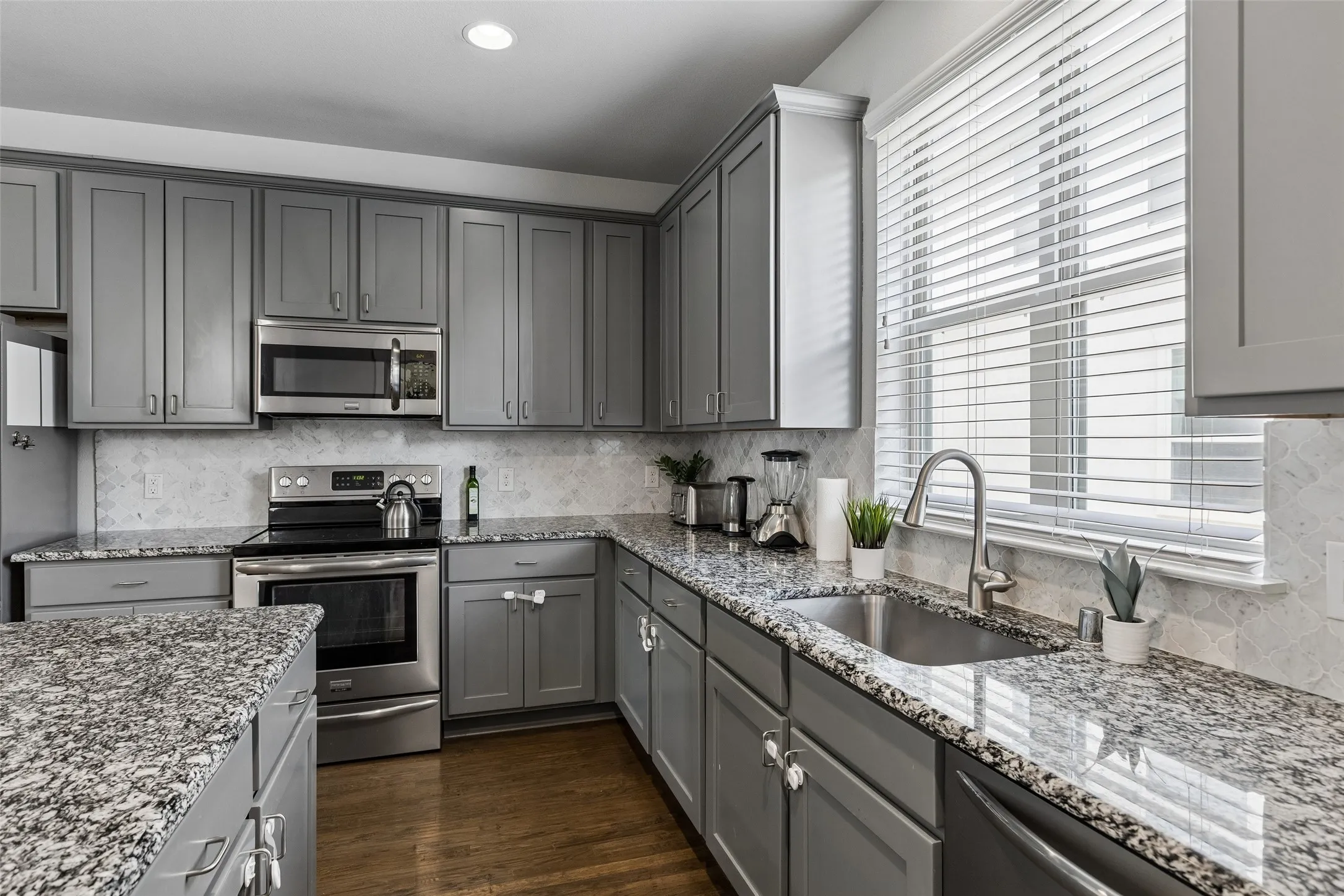 Gray cabinetry with stainless steel appliances, granite countertops, and a tile backsplash
