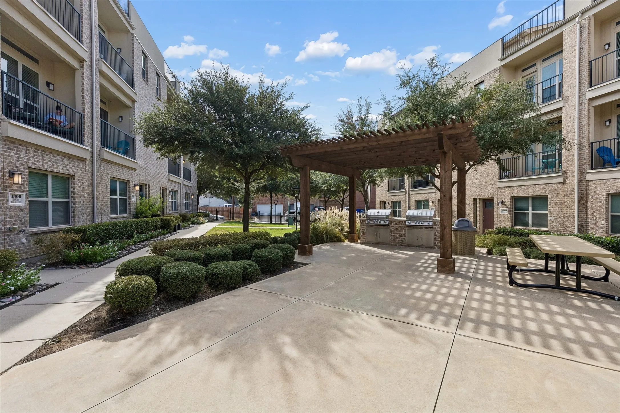 Outdoor entertaining area featuring a wood pergola, built-in grilling stations, a picnic table, and landscaped garden beds