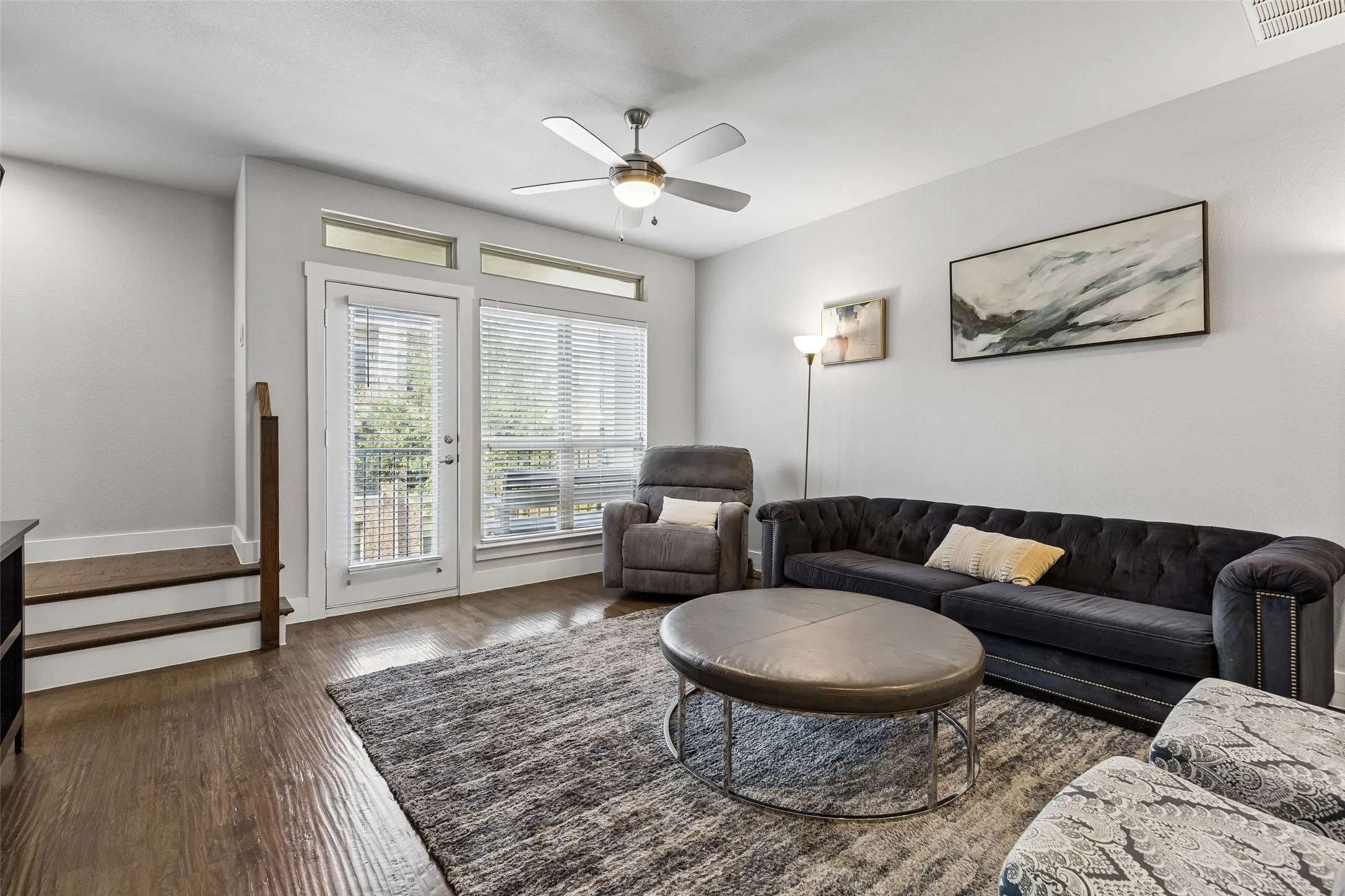 Hardwood-style flooring throughout, with a ceiling fan, white paneled door, and transom windows