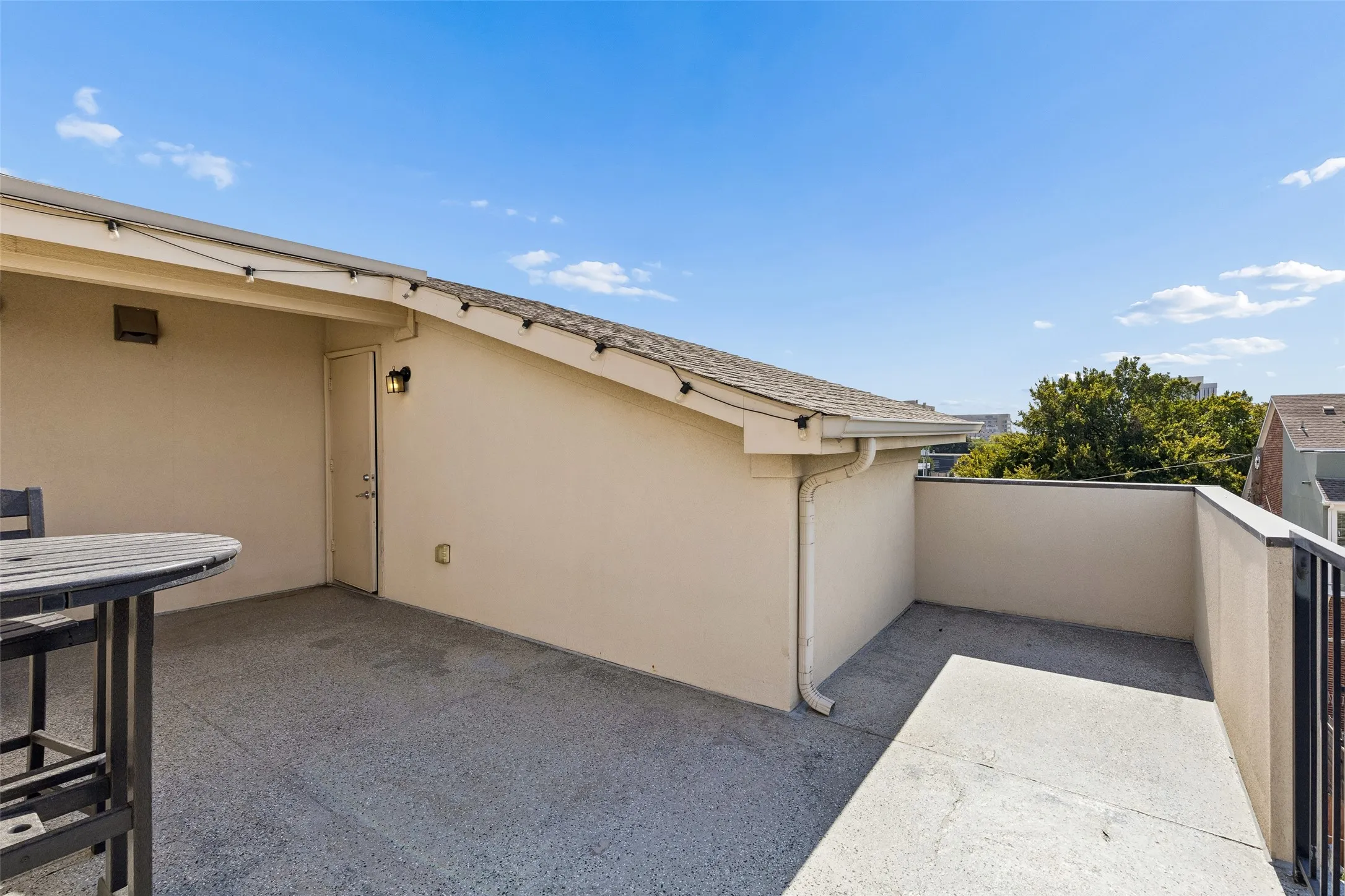 Outdoor patio with a stucco exterior, asphalt shingle roof, and a black metal railing