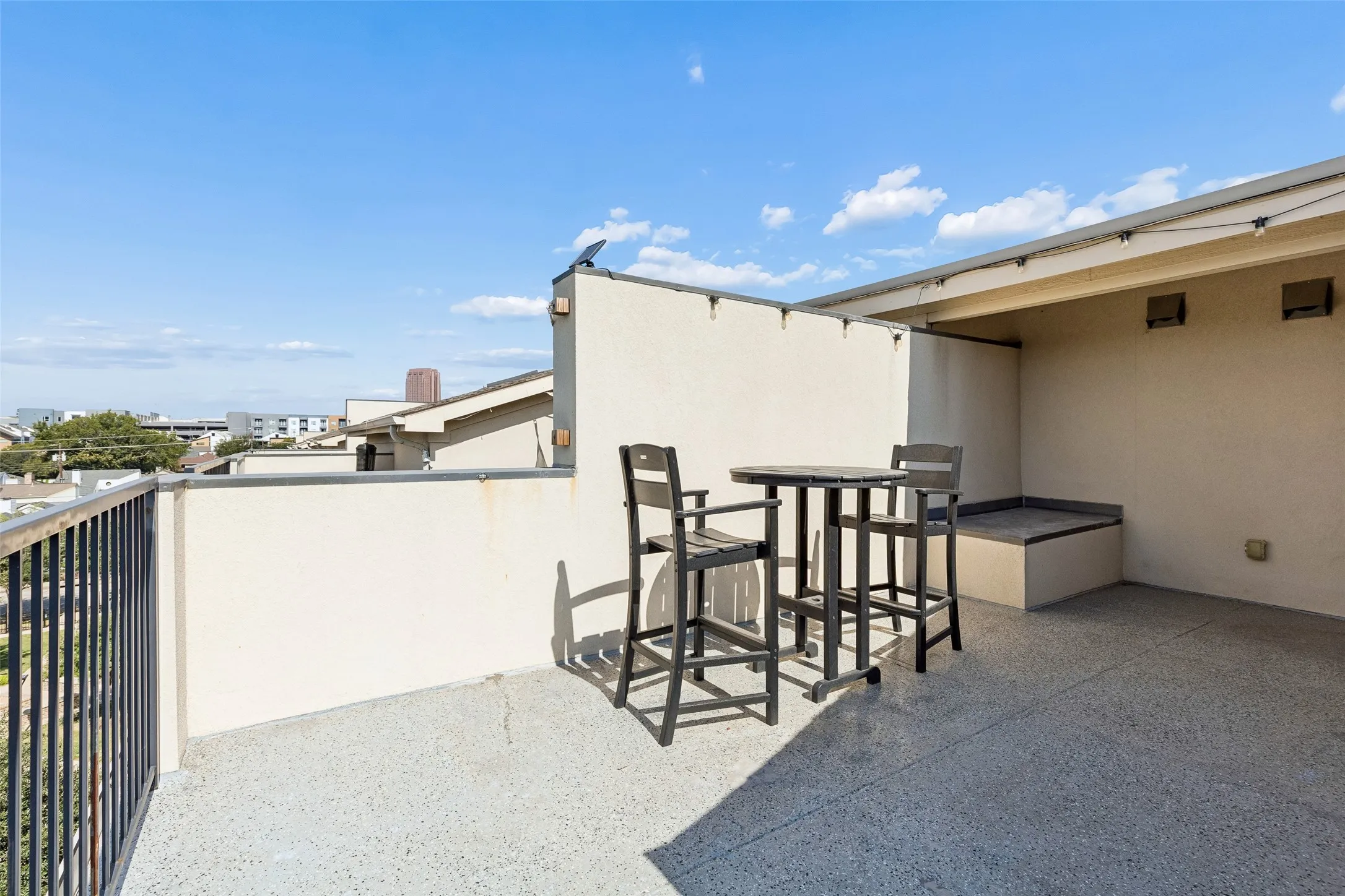 Rooftop patio featuring a built-in bench, string lighting, and black metal railing