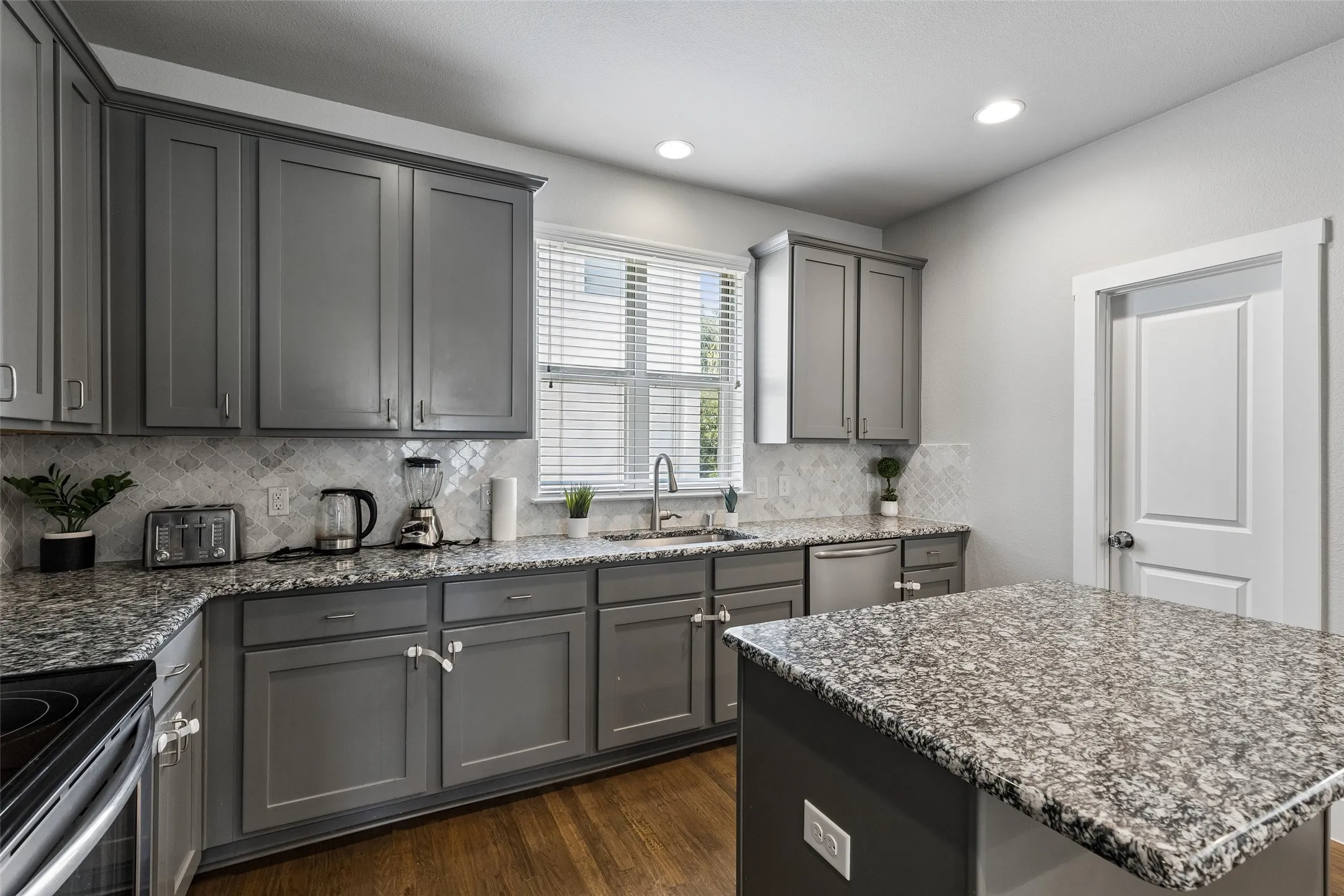 Kitchen featuring gray cabinetry, granite countertops, tile backsplash, stainless steel dishwasher, and wood-finish flooring