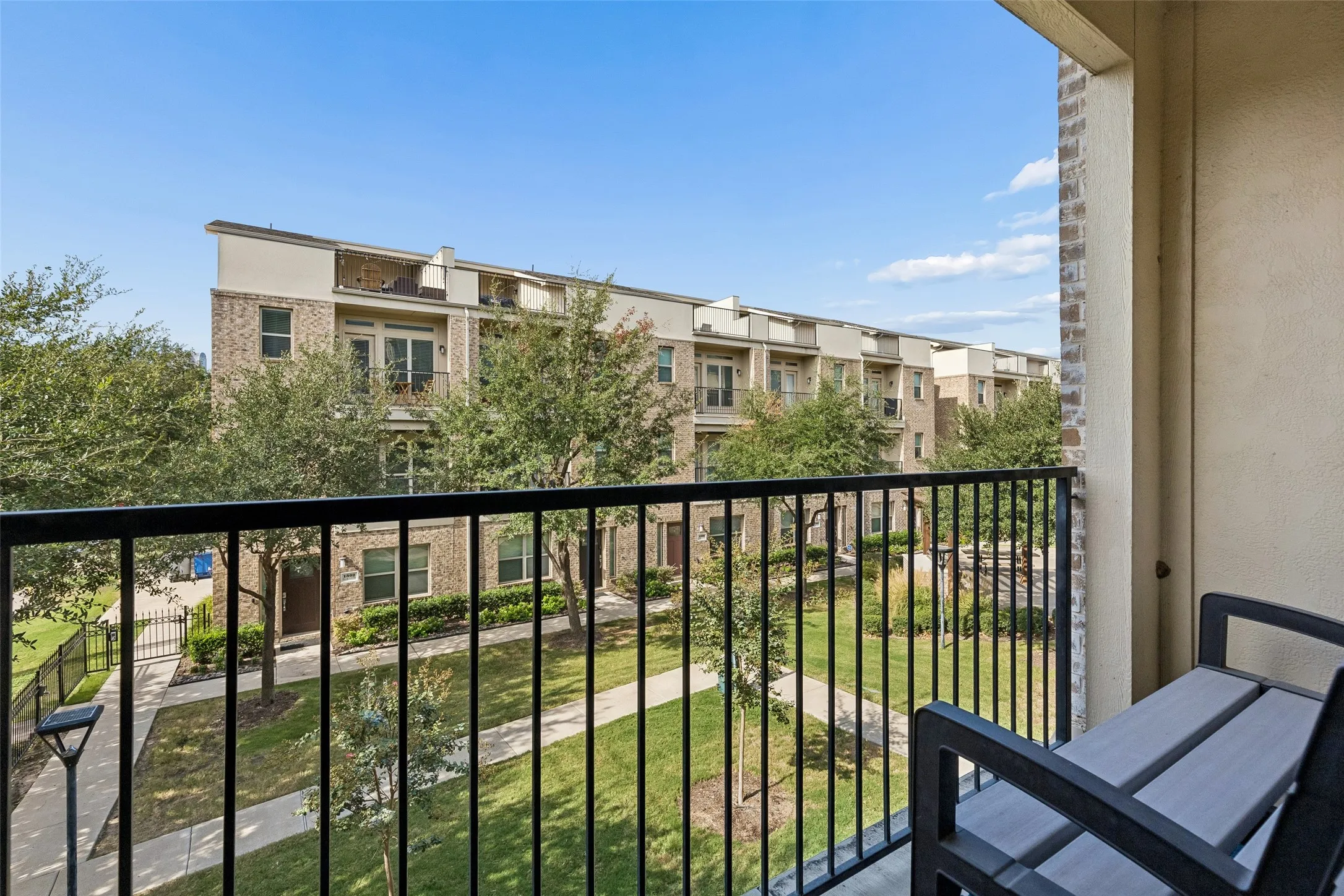 Balcony with black metal railing overlooking a community green space with paved walkways and mature trees