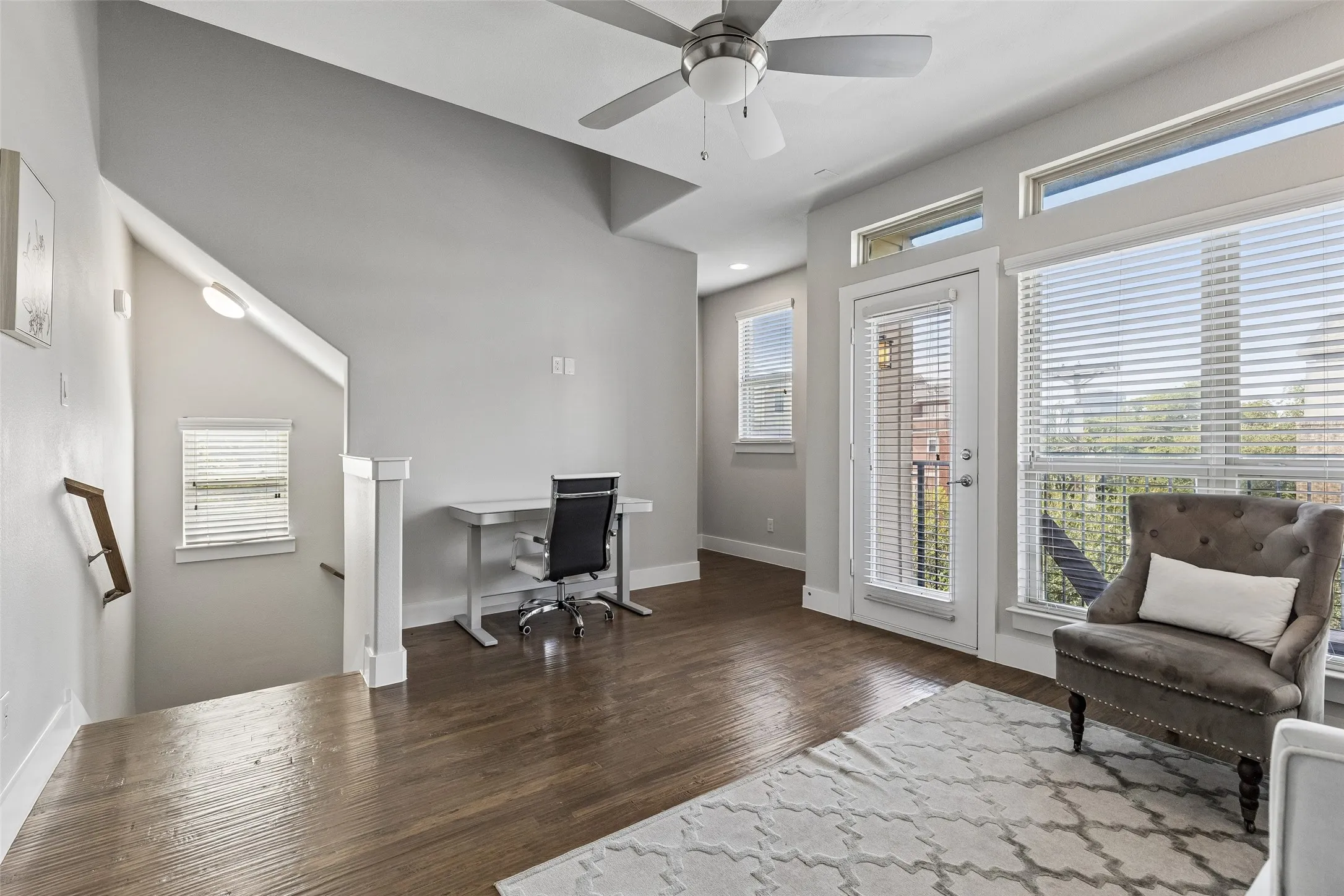 Hardwood flooring throughout, with a ceiling fan light fixture, multiple windows with blinds, and a glass-paneled door