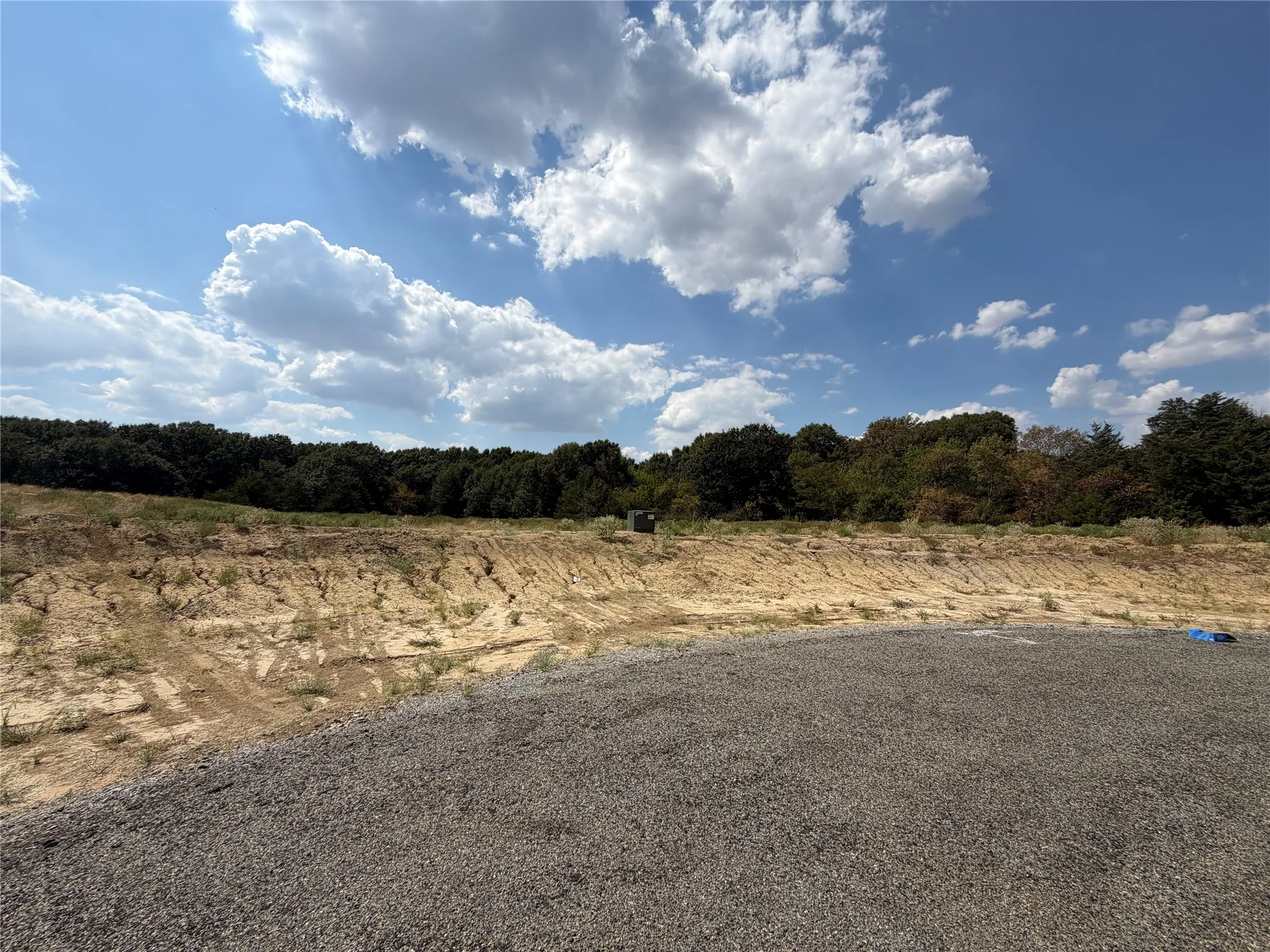 Gravel surface with a natural earth embankment and mature trees in the background