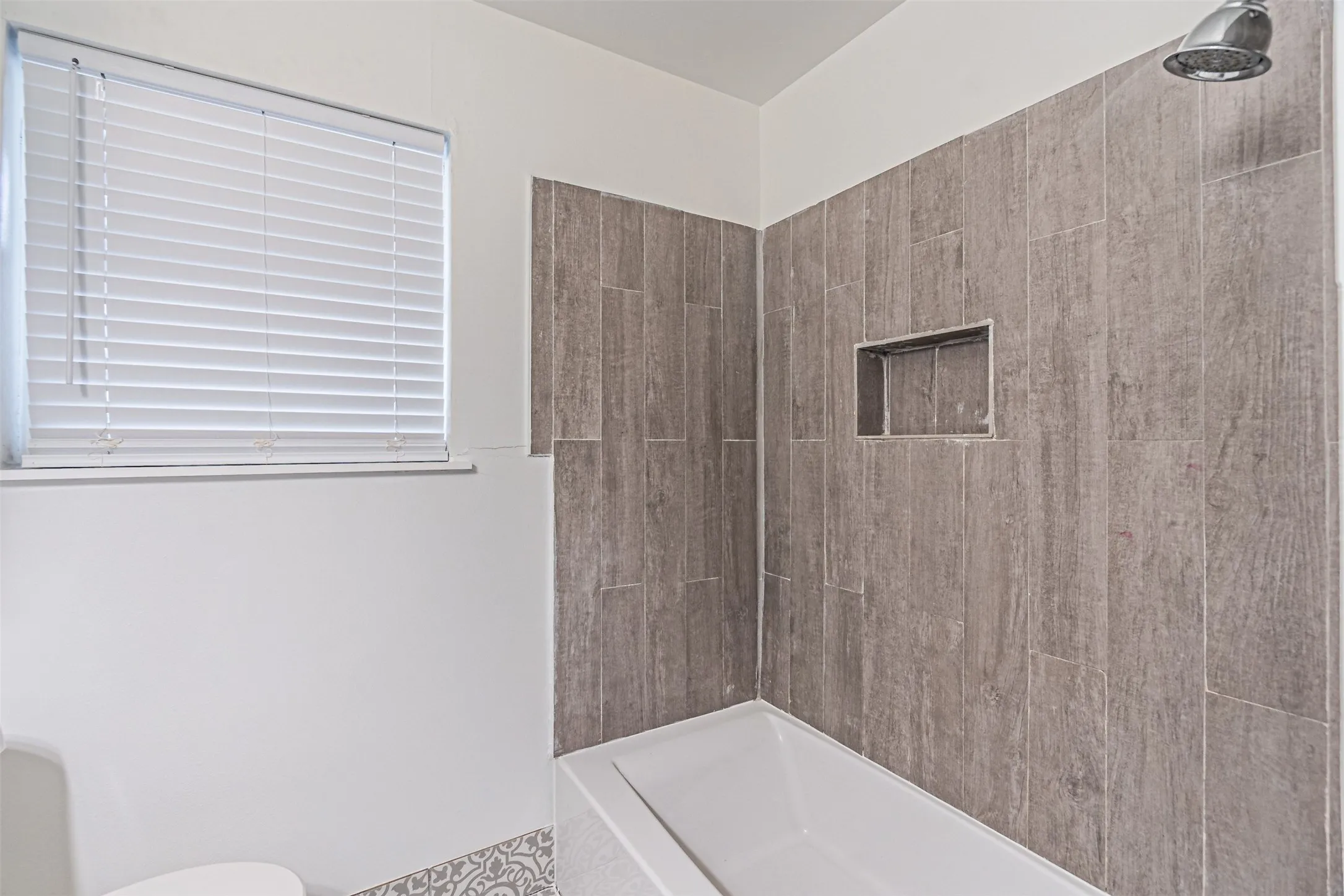 Bathtub with a tiled surround, shower niche, and shower head