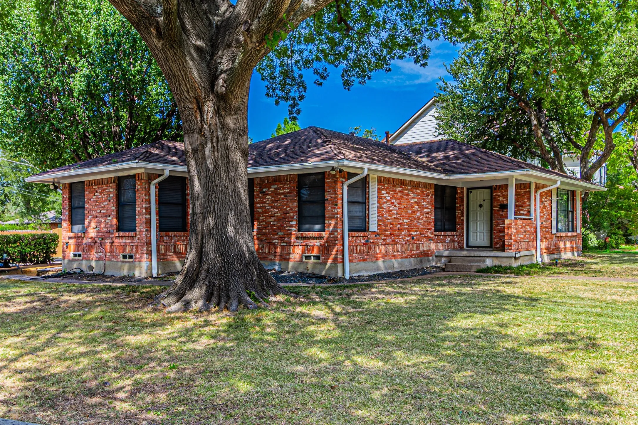Brick exterior with white trim, covered front entry, and a mature tree