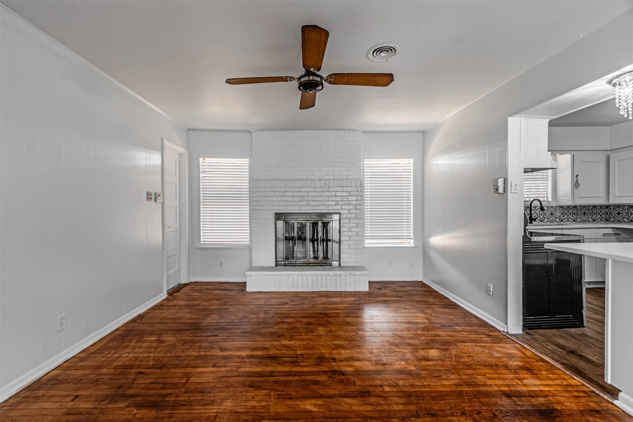 Wood-finish flooring, white paneling, and a painted brick fireplace with hearth