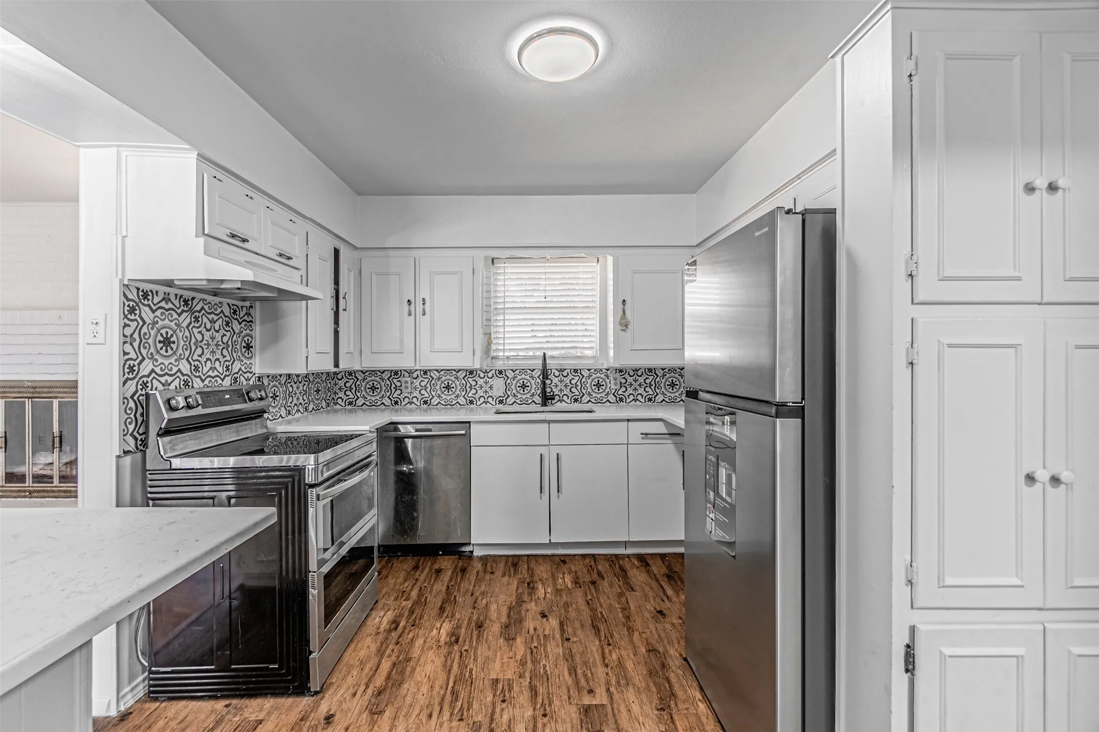Kitchen featuring wood-finish flooring, white cabinetry, a patterned tile backsplash, stainless steel appliances, and a built-in pantry